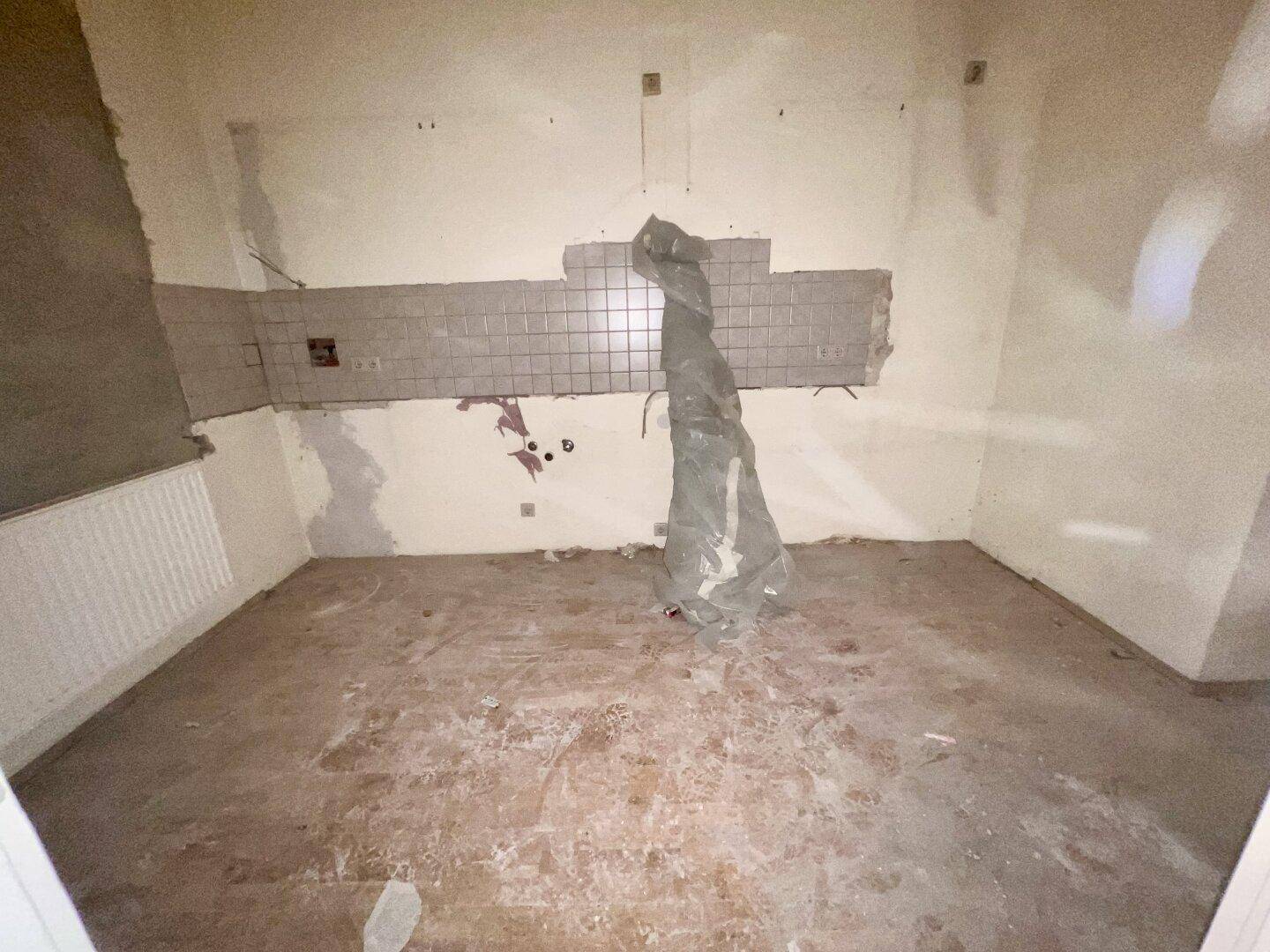 Leere Küche in Renovierung mit Fliesen an der Wand und Anschlüssen für zukünftige Geräte.