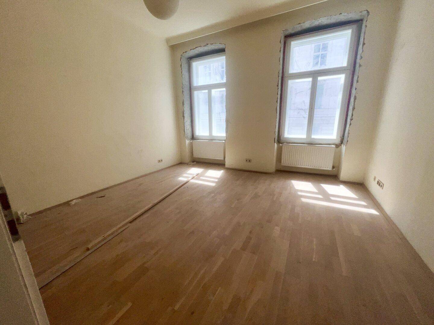 Heller, leerer Raum mit zwei großen Fenstern und Holzboden, ideal für individuelle Gestaltungsmöglichkeiten.
