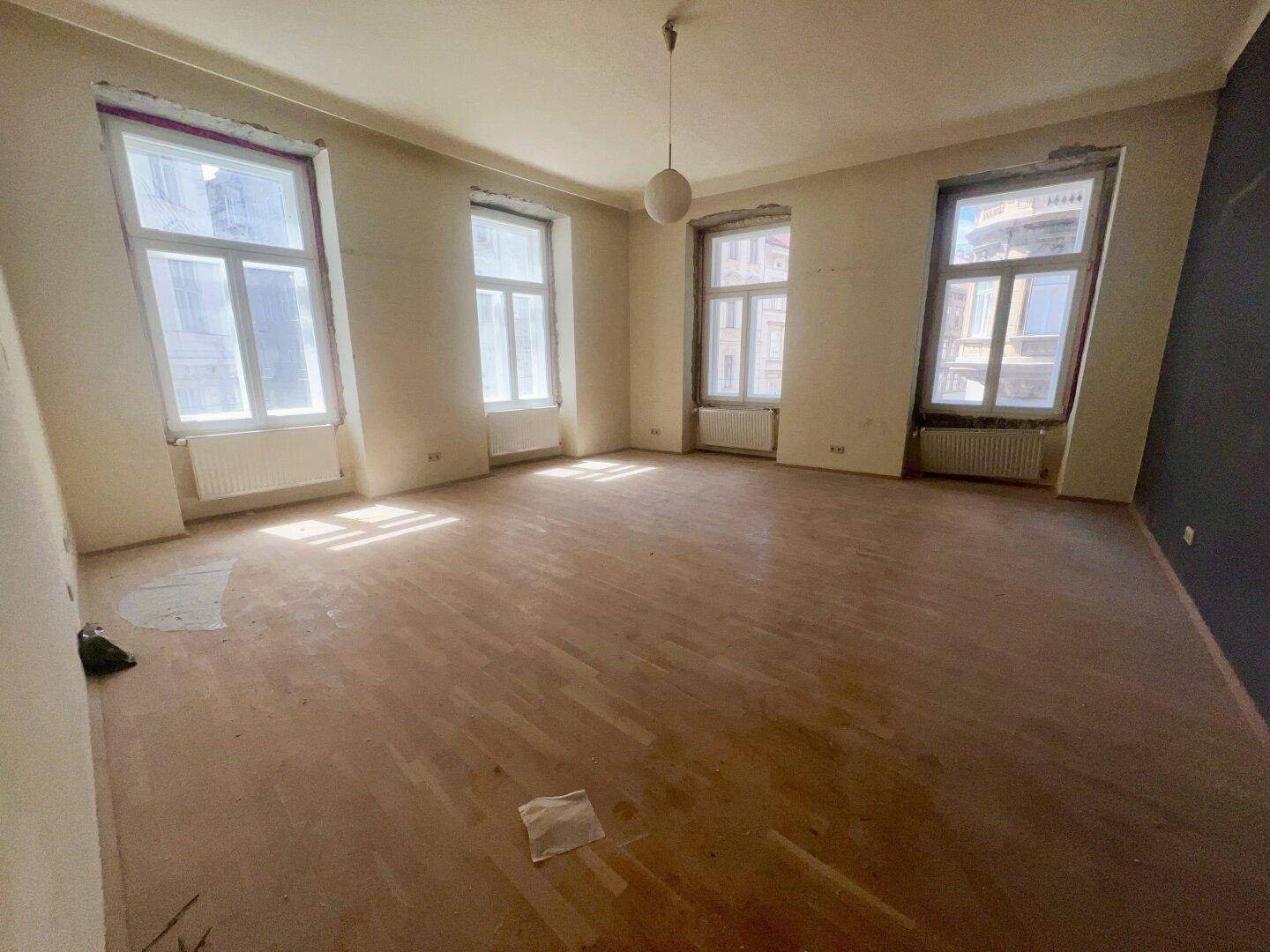 Geräumiger, unmöblierter Raum mit großen Fenstern und Holzboden, bereit zur Renovierung und Gestaltung.