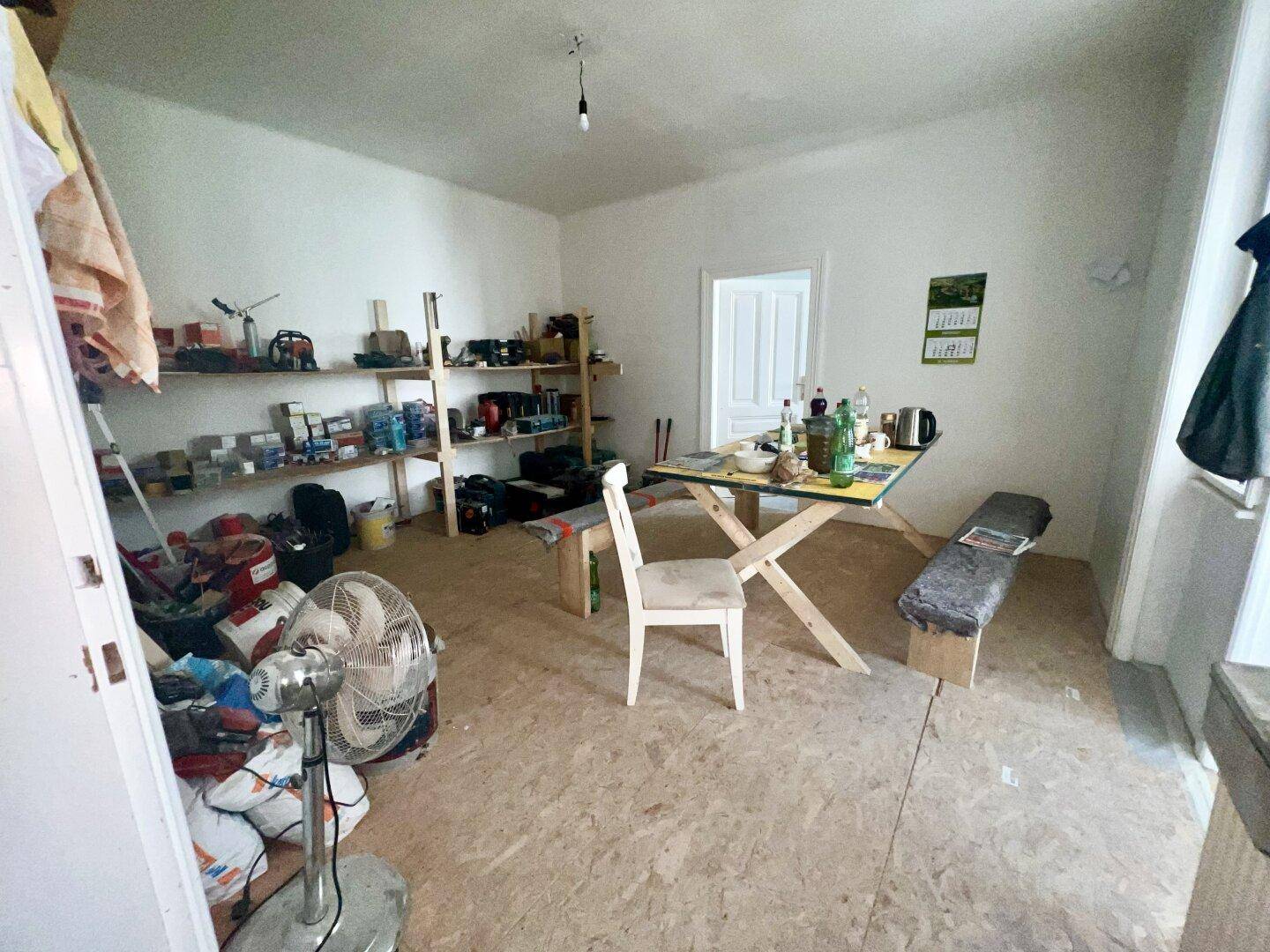 Unklarer Raum im Renovierungszustand mit provisorischen Möbeln und Lagerregalen.