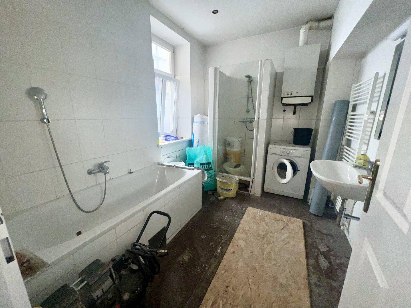 Badezimmer im Renovierungszustand mit Badewanne, Dusche, Waschbecken und Waschmaschine.