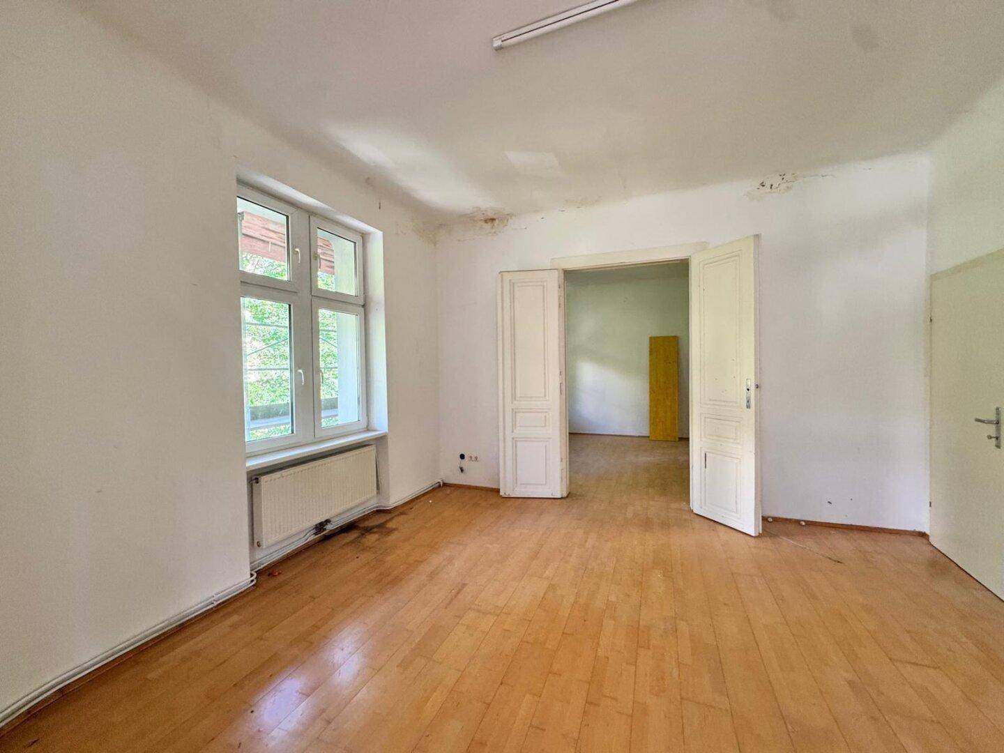 Geräumiger Wohnbereich mit Parkettboden und Zugang zu einem weiteren Zimmer.