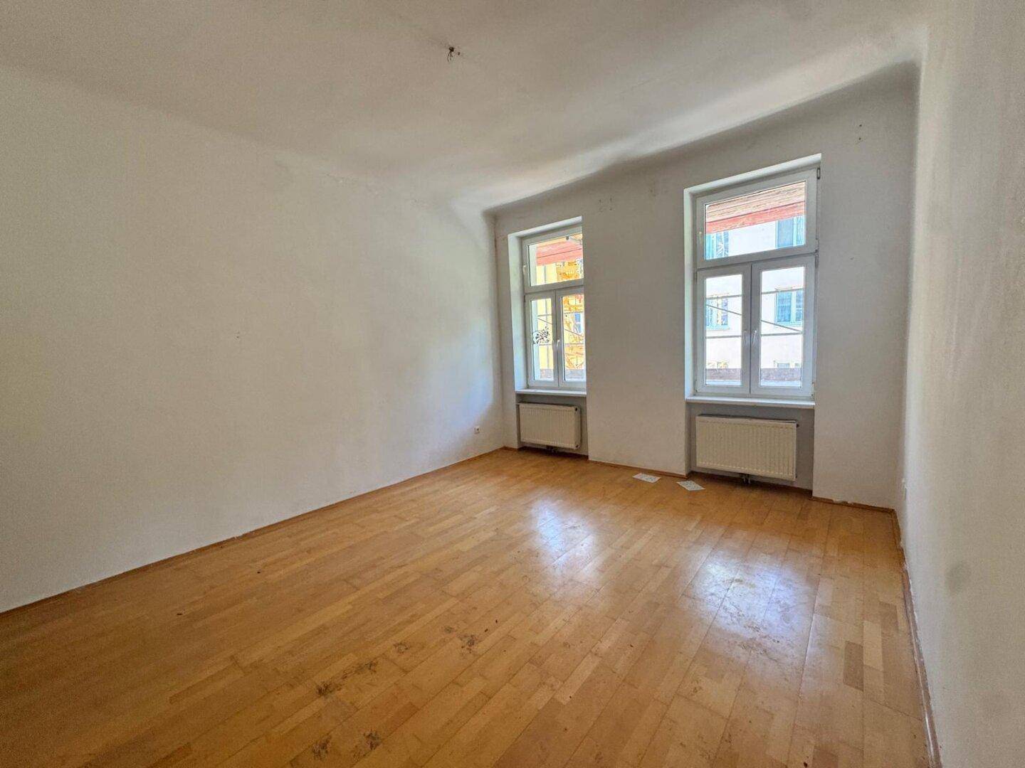 Leerer Raum mit Holzboden und zwei Fenstern, ideal für individuelle Gestaltung.