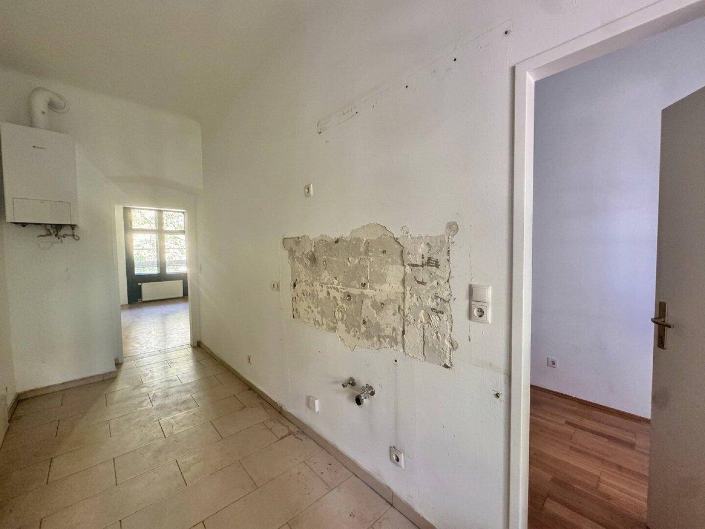 Unfertige Küche mit sichtbaren Anschlüssen und einem Heizkessel an der Wand.