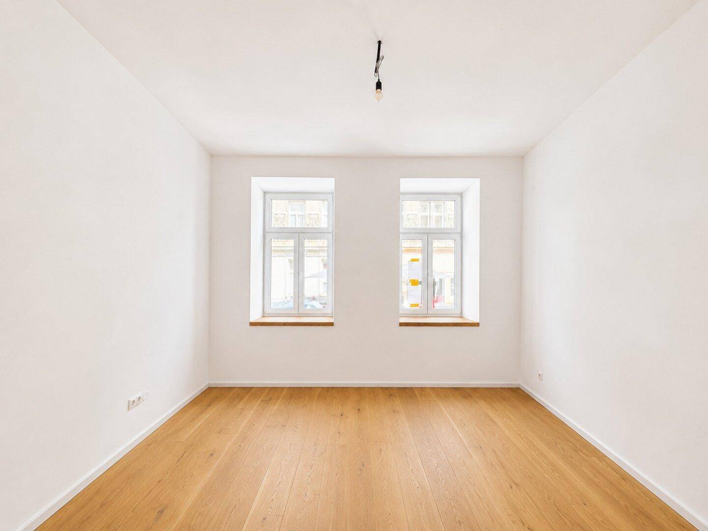 Geräumiger, heller Raum mit zwei Fenstern und elegantem Holzparkettboden, bereit zur individuellen Gestaltung.
