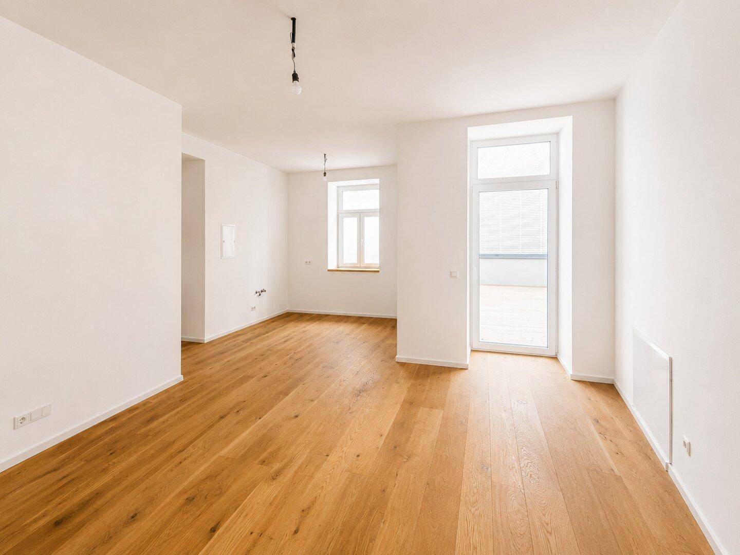 Heller, leerer Raum mit neuem Holzparkettboden und Zugang zu einem Balkon oder einer Terrasse.
