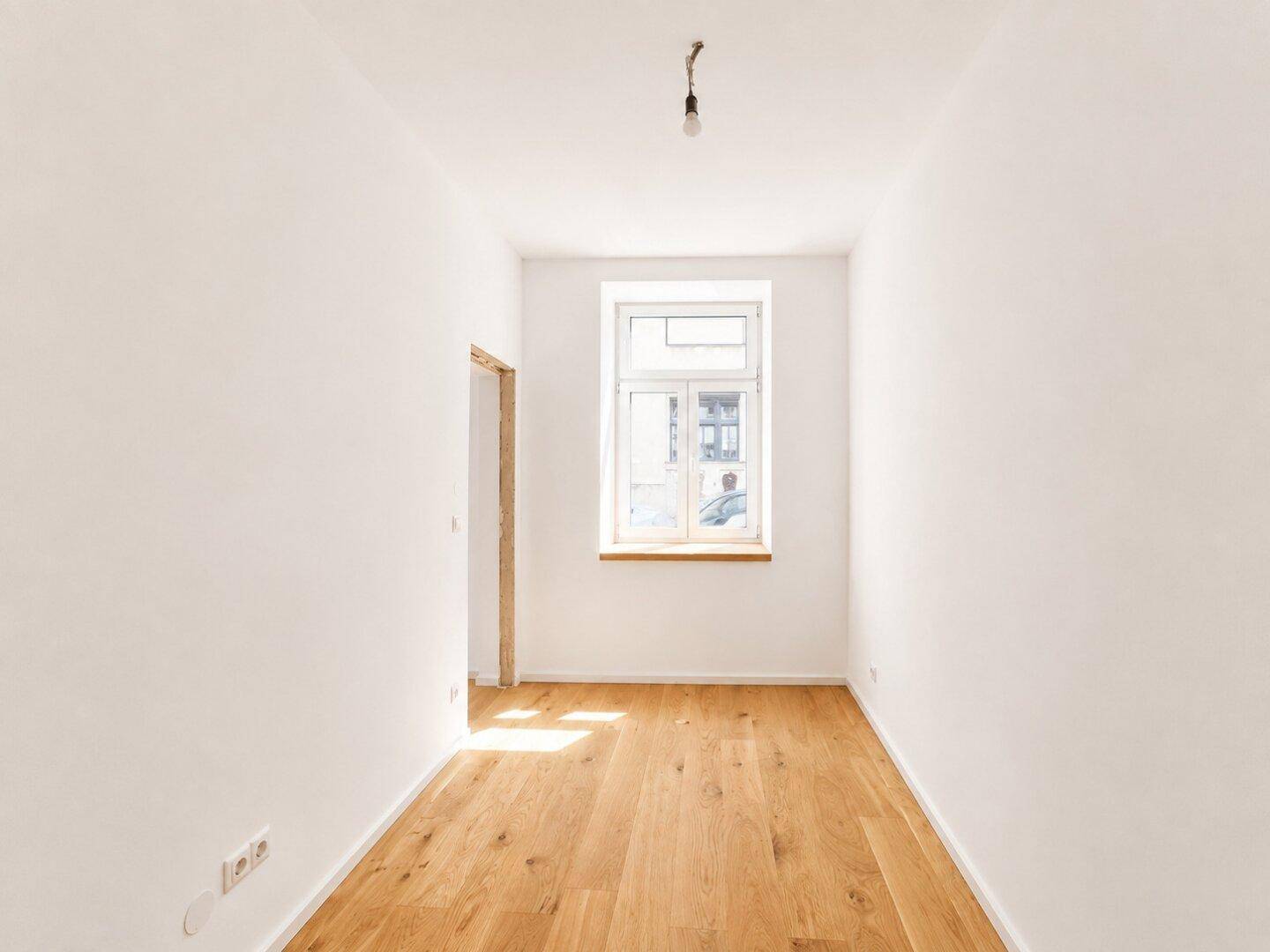 Schmales, helles Zimmer mit Holzboden und einem Fenster, perfekt als Schlafzimmer oder Büro nutzbar.