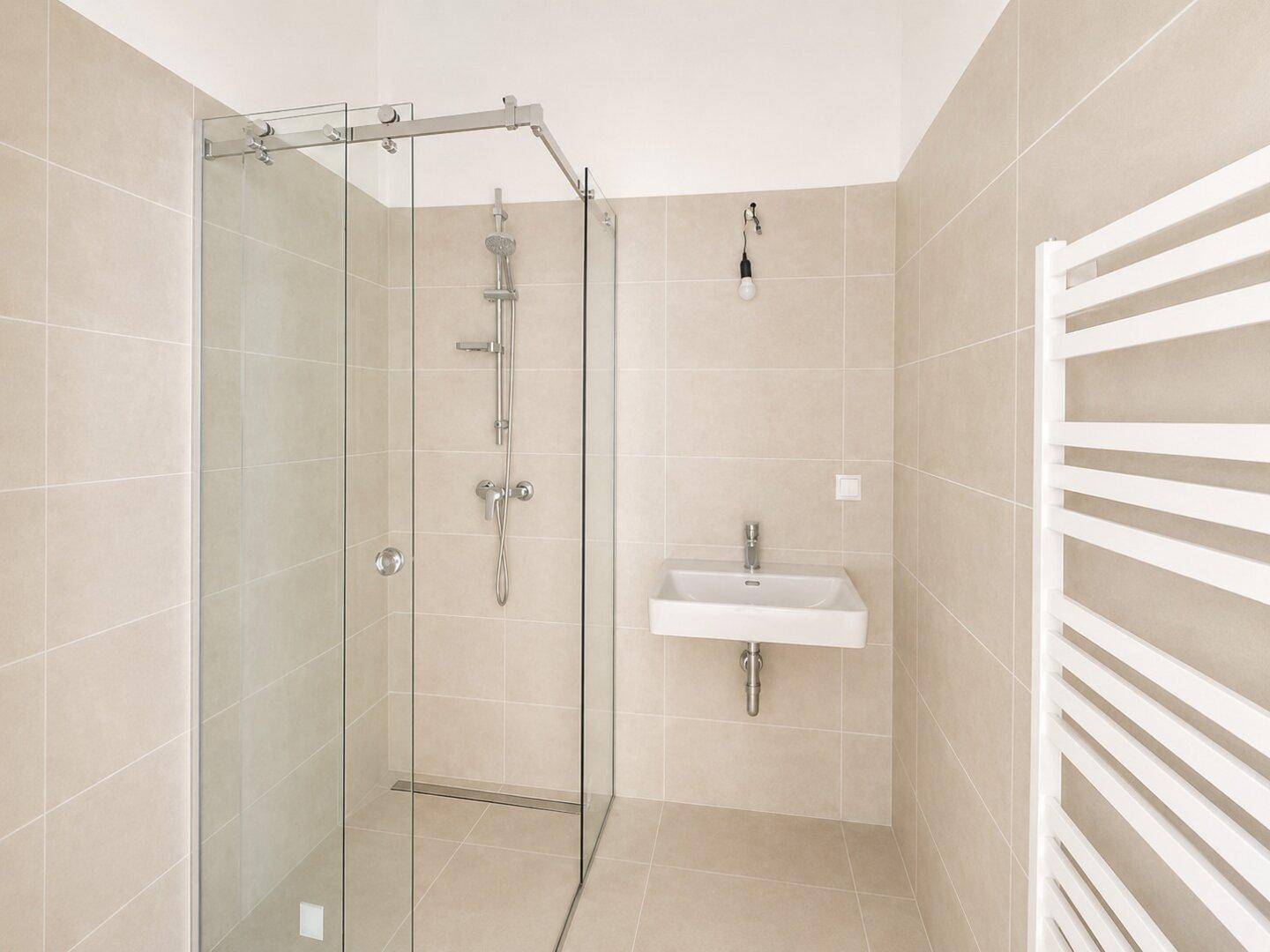 Modernes Badezimmer mit begehbarer Glasdusche, wandhängendem Waschbecken und beigefarbenen Fliesen, inklusive Handtuchheizkörper.
