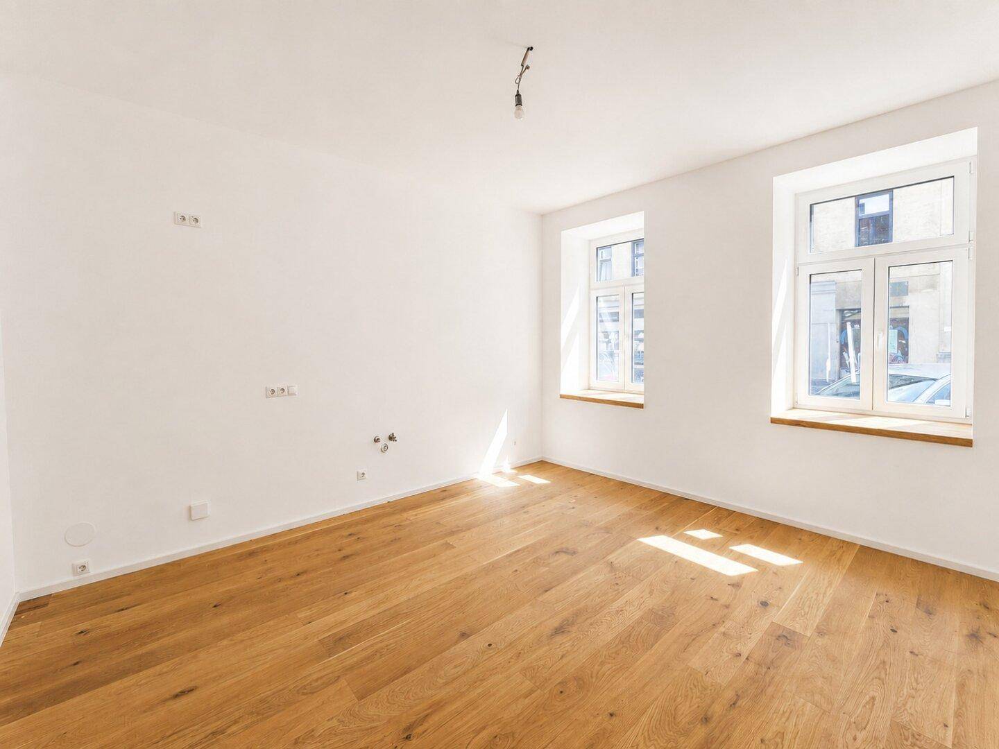 Lichtdurchfluteter Raum mit frisch verlegtem Holzboden und hellen Wänden, ideal für vielfältige Nutzung.