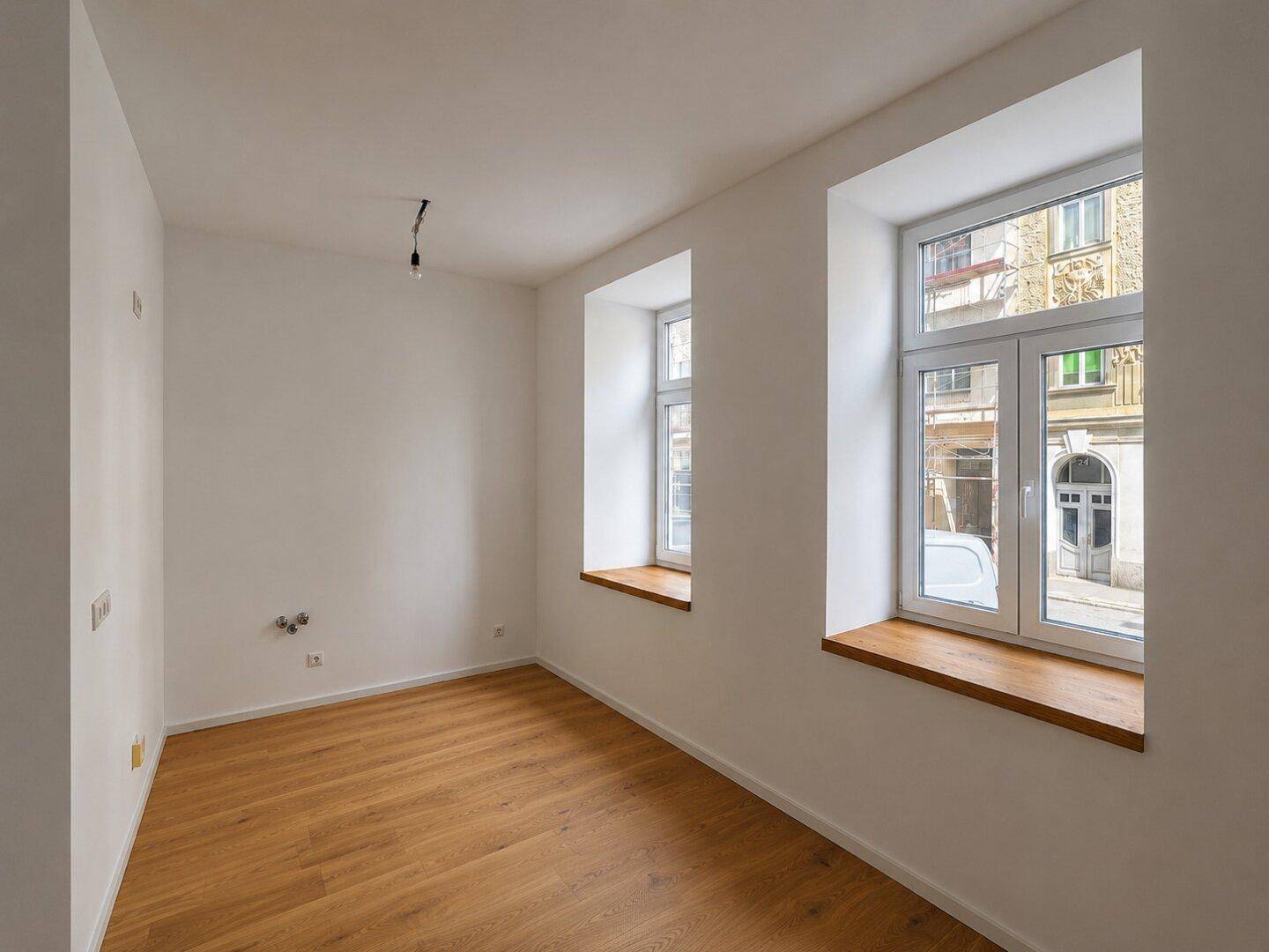 Lichtdurchfluteter Raum mit elegantem Parkettboden und großen Fenstern, die viel Tageslicht hereinlassen.