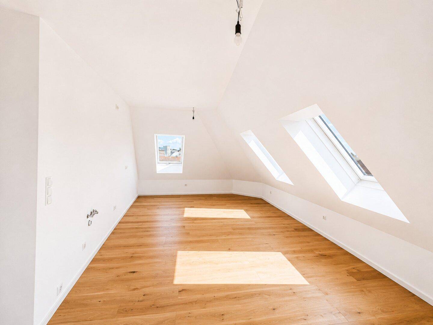 Geräumiges Dachgeschosszimmer mit schrägen Wänden, Holzboden und hellen Dachfenstern.