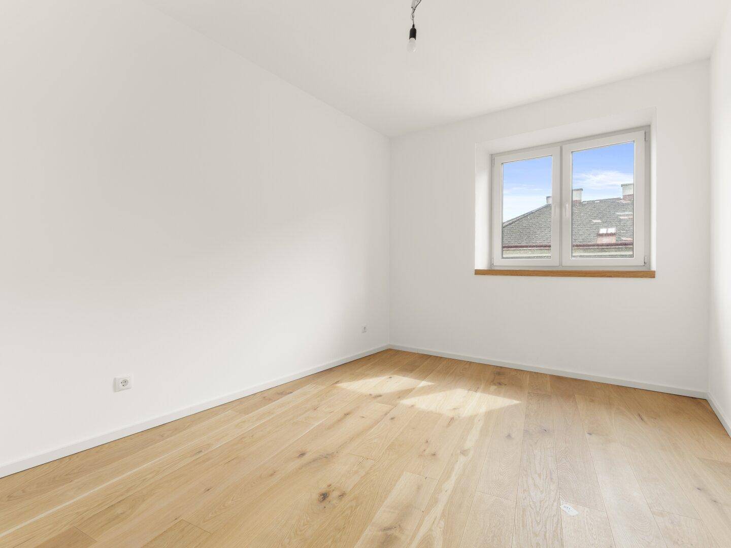 Helles Schlafzimmer mit Holzboden und einem Fenster, das viel Tageslicht hereinlässt.