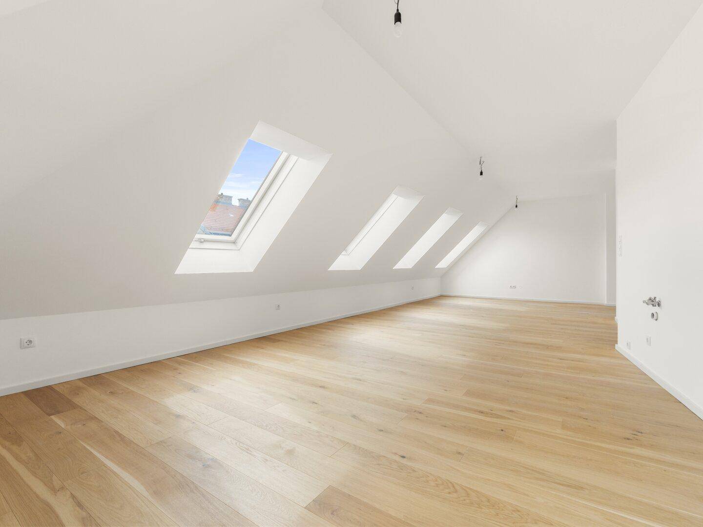 Weitläufiger Dachgeschossraum mit Holzboden und mehreren Dachfenstern, die den Raum erhellen.