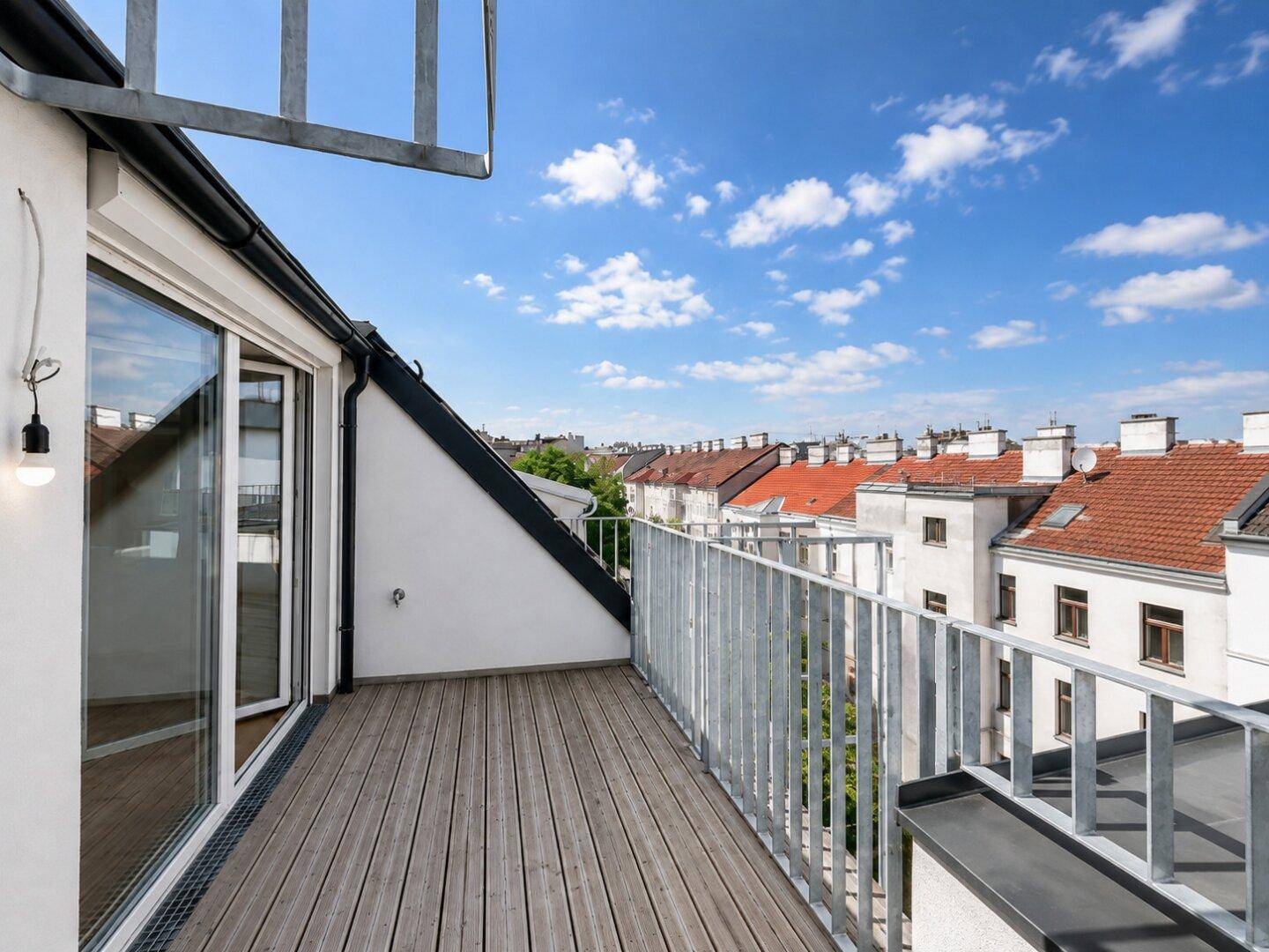 Geräumiger Balkon mit Holzboden und Metallgeländer, bietet einen weiten Blick über die Dächer der Stadt.