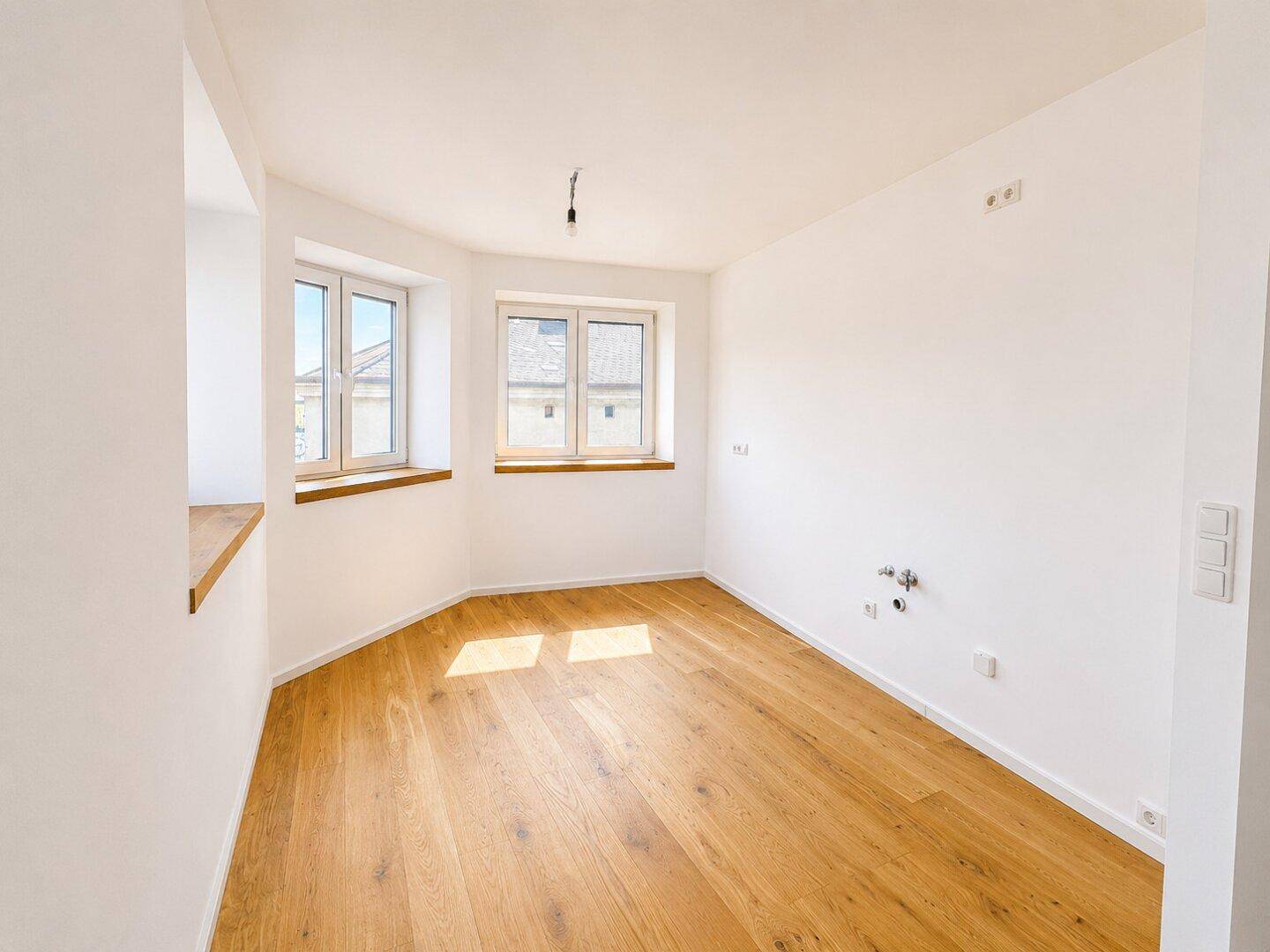 Helles Zimmer mit Holzboden und Anschlüssen für Waschmaschine oder Spüle, ideal als Hauswirtschaftsraum.