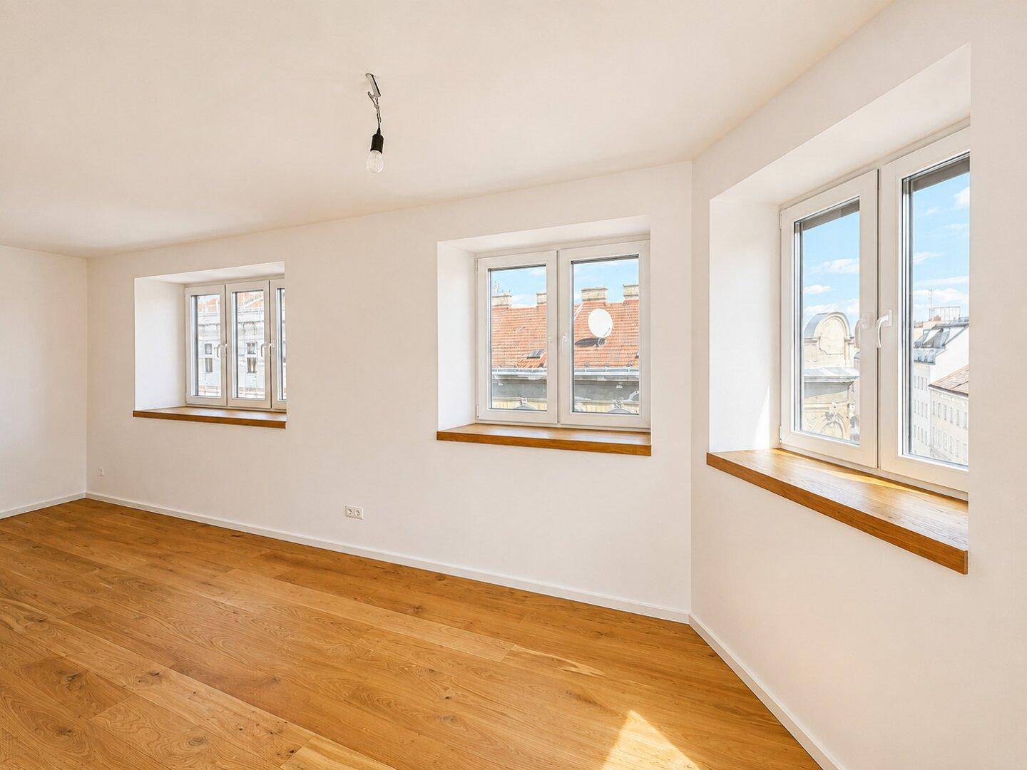 Geräumiges, helles Zimmer mit Parkettboden und Blick auf die umliegenden Dächer und Gebäude.