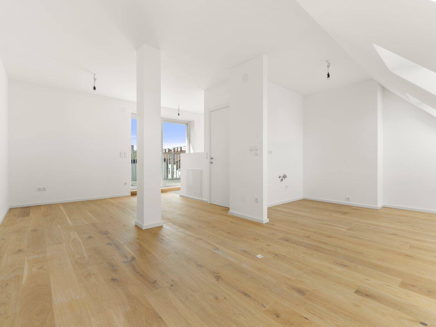 Geräumiger Wohnbereich mit Holzboden, weißen Wänden und Zugang zu einem Balkon.