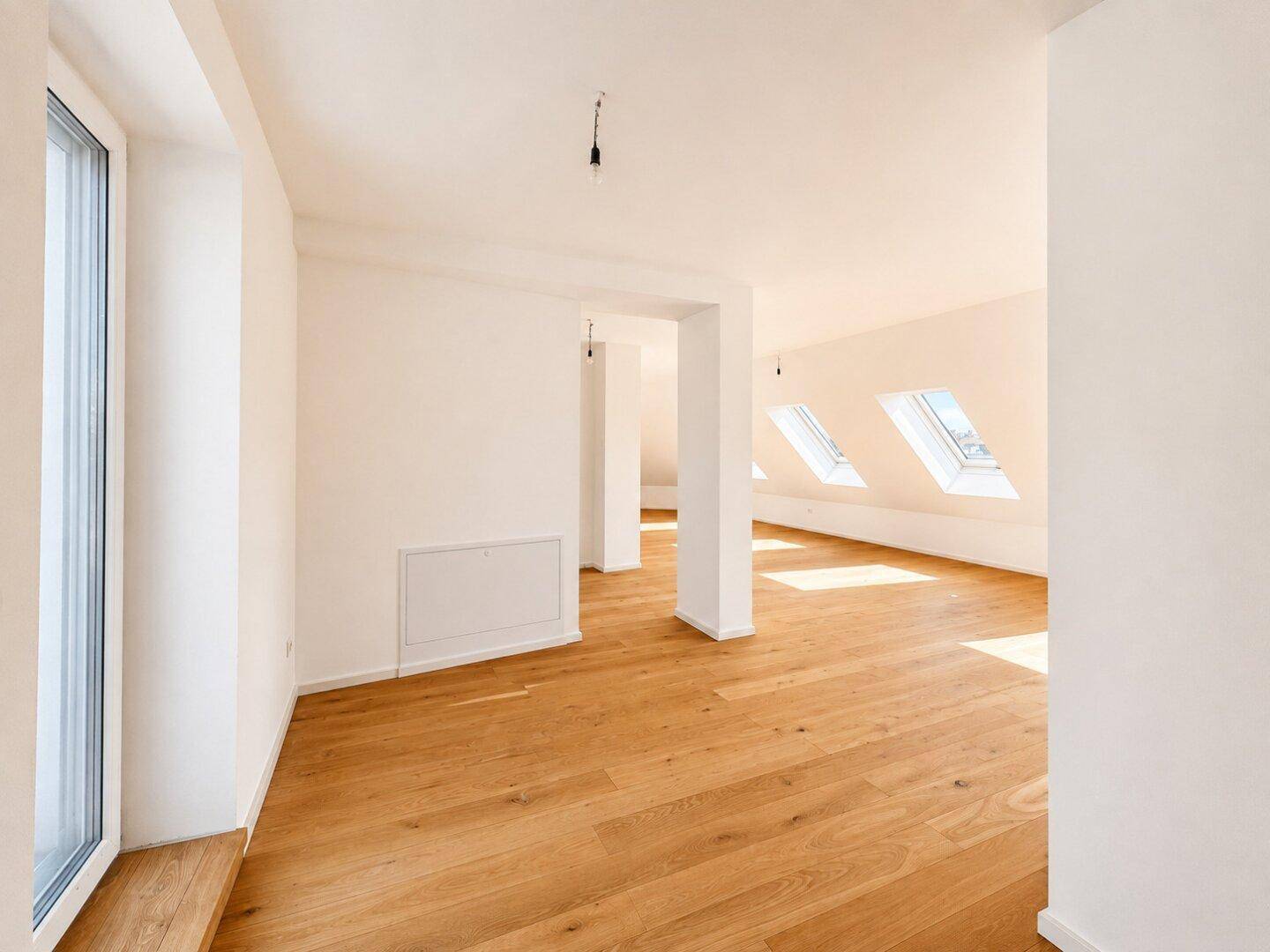 Heller Wohnraum mit Holzboden, weißen Wänden und mehreren Dachfenstern für viel Tageslicht.