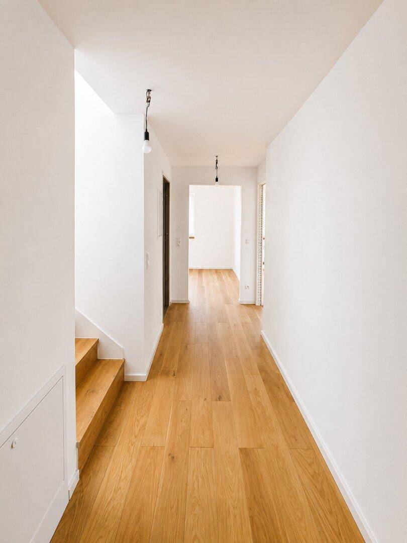 Heller Flur mit Holzboden und einer modernen Holztreppe, die in die obere Etage führt.