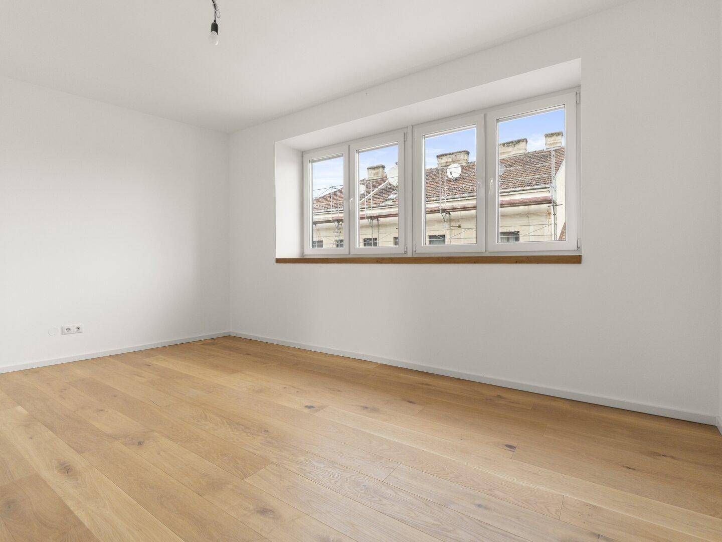 Leerer Raum mit Holzboden und einem Fenster, das einen Blick auf die umliegenden Dächer ermöglicht.