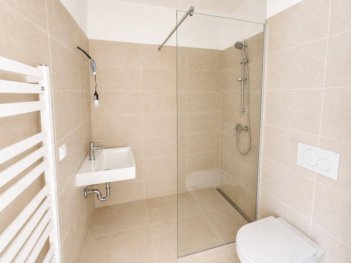 Modernes Badezimmer mit beigefarbenen Fliesen, ebenerdiger Dusche und wandhängendem WC.