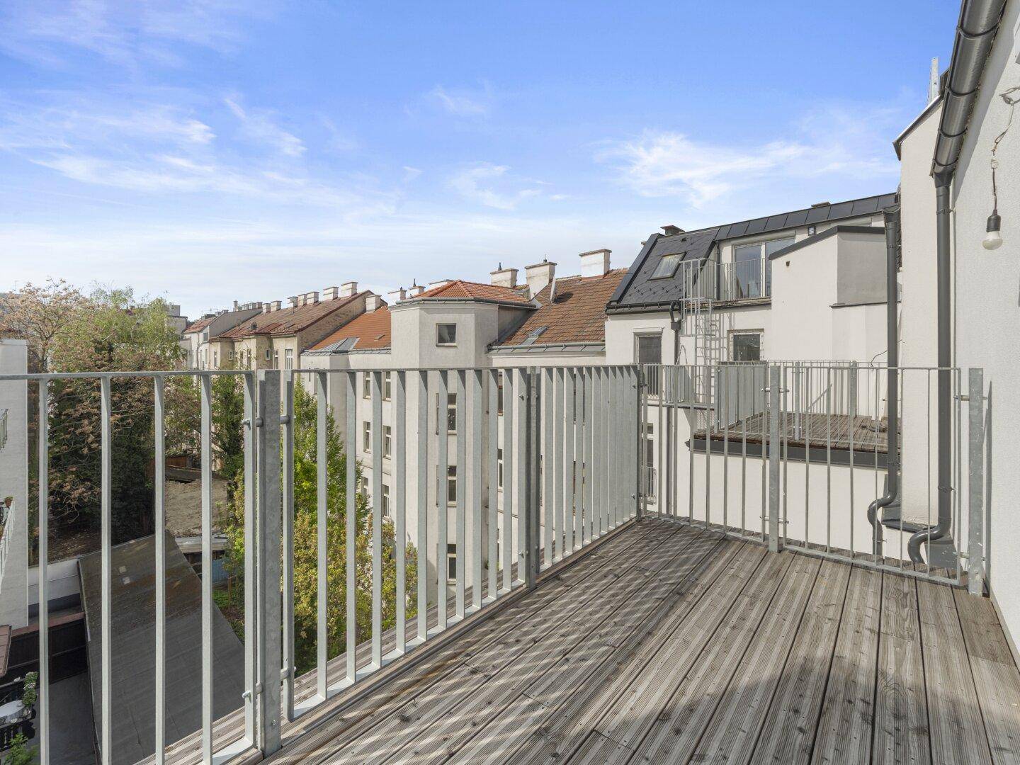 Geräumiger Balkon mit Holzboden und Blick auf die umliegenden Dächer und Gebäude.