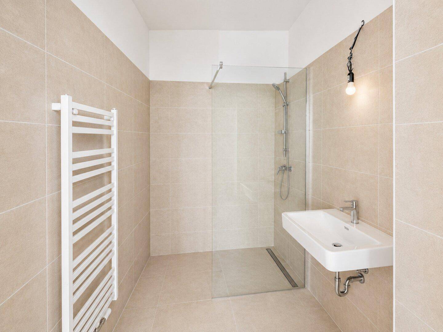 Helles Badezimmer mit beigefarbenen Fliesen, moderner Dusche und beheiztem Handtuchhalter.