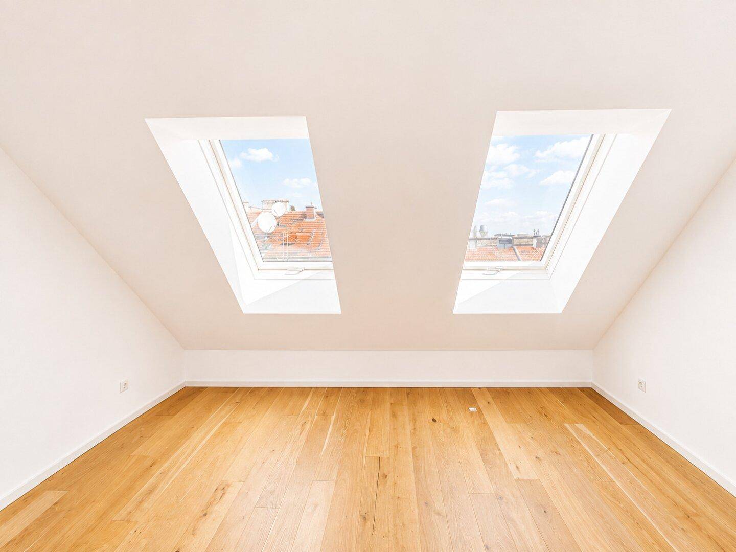 Heller Dachraum mit Holzboden, Dachschrägen und zwei großen Dachfenstern für viel Licht.