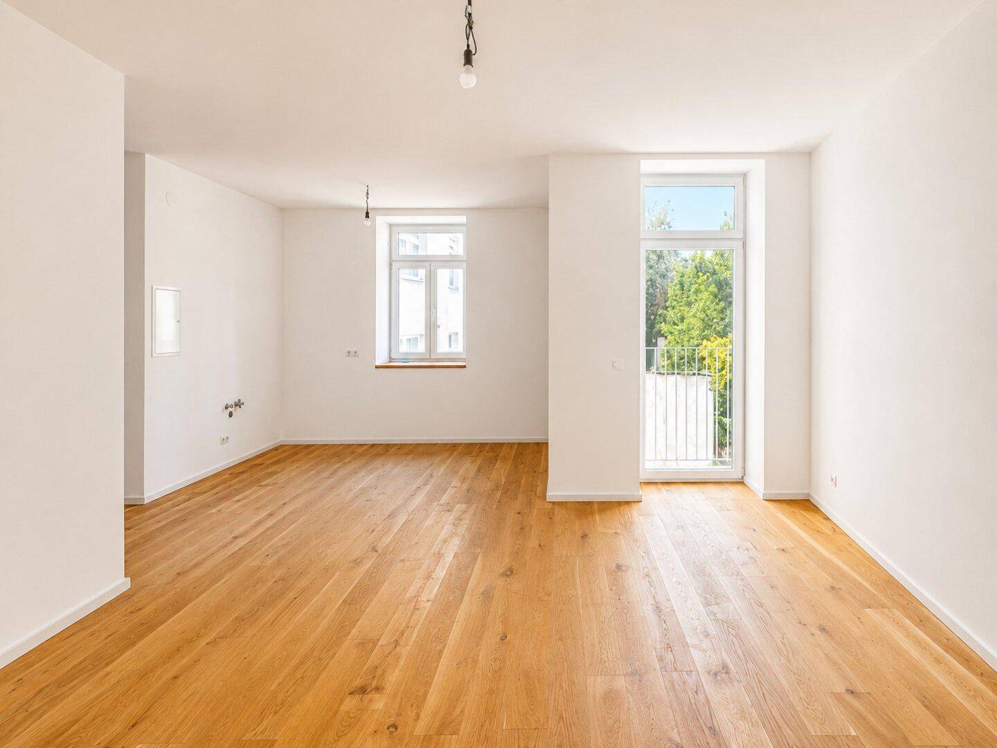 Geräumiger, leerer Wohnbereich mit Holzboden und Zugang zu einem französischen Balkon.