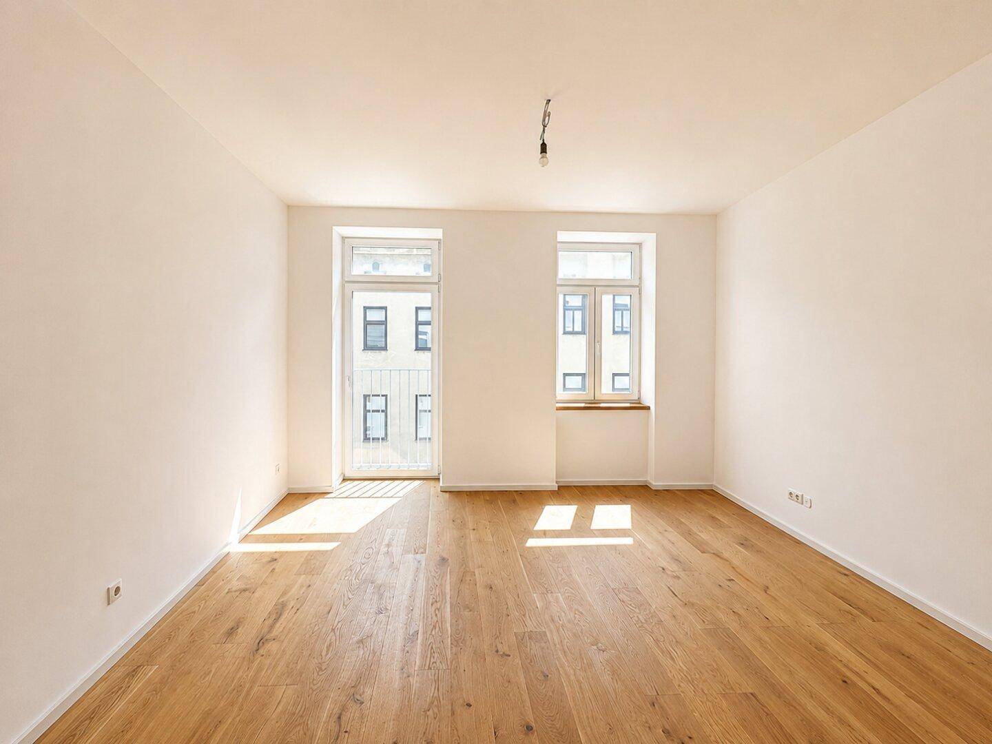 Lichtdurchfluteter Raum mit Holzboden und großen Fenstern, die viel Sonnenlicht hereinlassen.