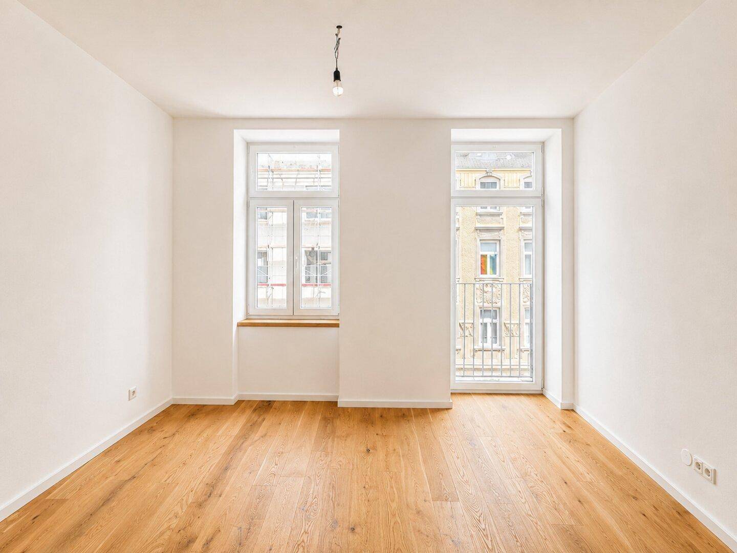 Heller Raum mit Holzboden, hohen Fenstern und Zugang zu einem französischen Balkon.
