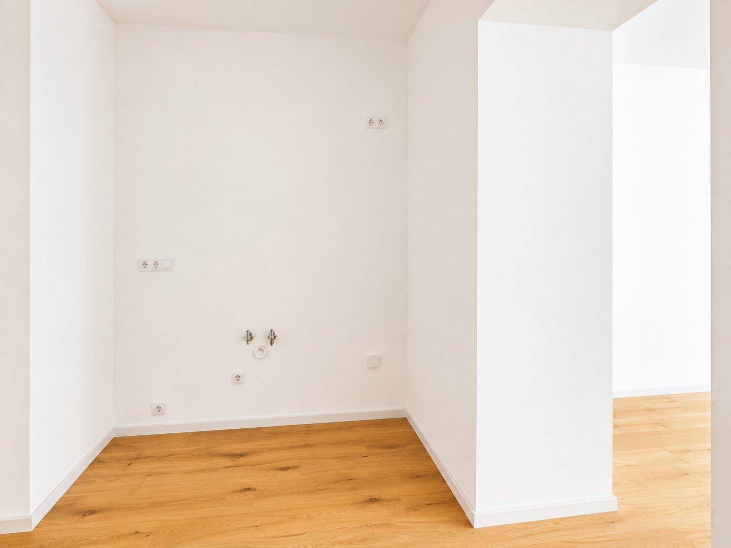 Leerer Küchenbereich mit Anschlüssen für eine zukünftige Einbauküche und Holzboden.