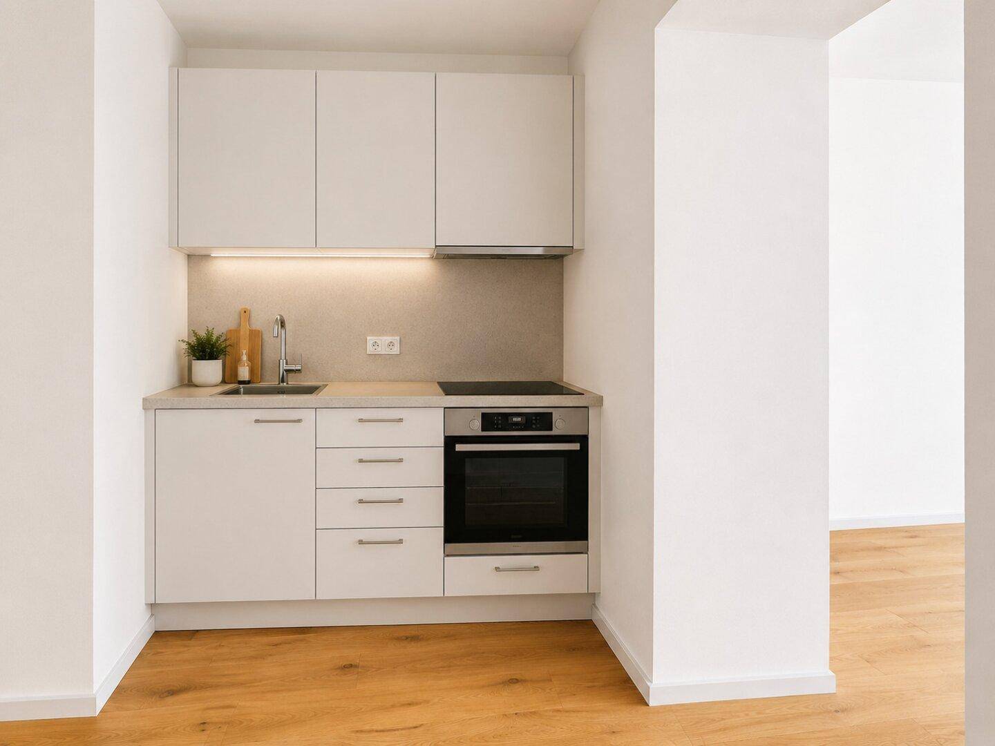 Moderne, kompakte Küchenzeile mit weißen Schränken, Induktionskochfeld und integriertem Backofen.