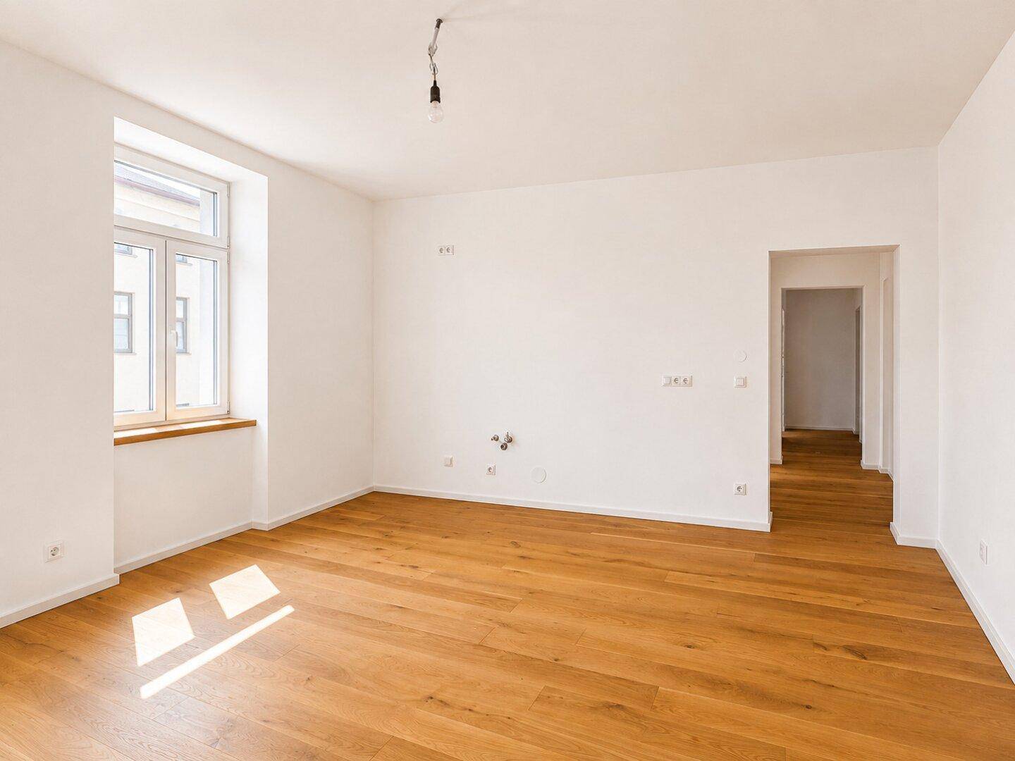 Heller Raum mit Parkettboden und Fenster, vorbereitet für Kücheninstallationen in einem offenen Wohnbereich.