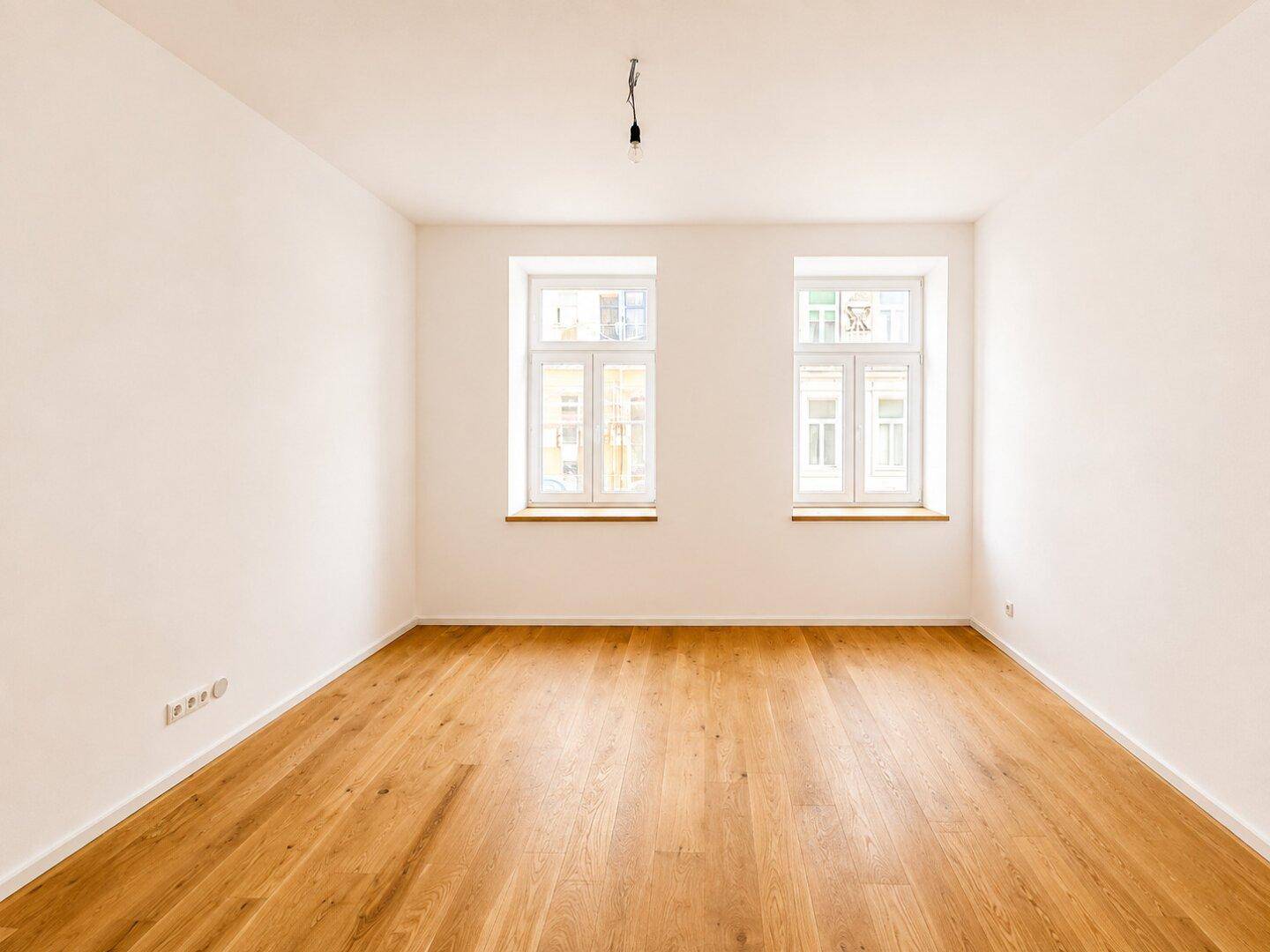 Lichtdurchfluteter Raum mit Holzboden und zwei großen Fenstern, bereit zur individuellen Gestaltung.