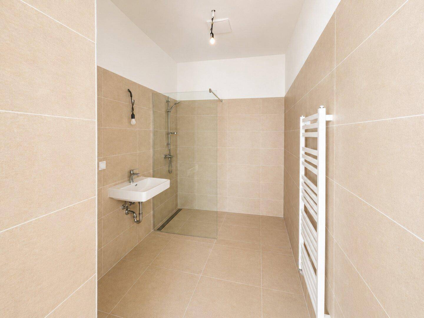 Modernes Badezimmer mit beigefarbenen Fliesen, ebenerdiger Dusche und Handtuchheizkörper.