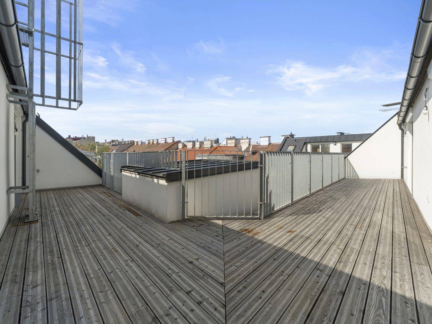 Geräumige Dachterrasse mit Holzboden und Blick über die Dächer der Stadt, ideal zum Entspannen.