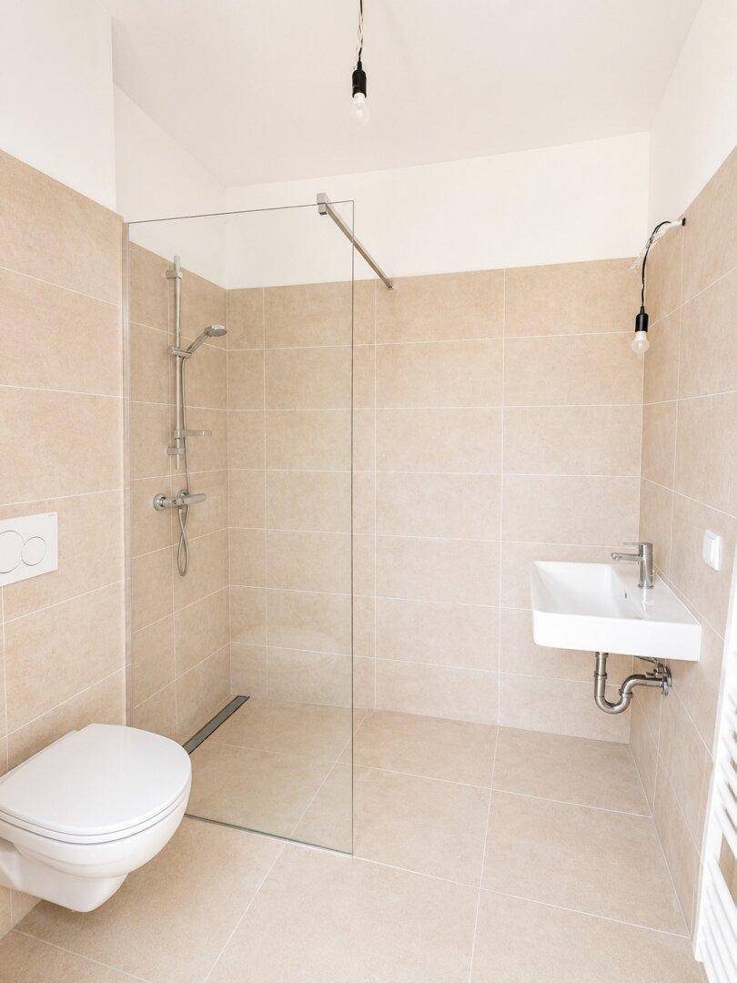Modernes Badezimmer mit beigefarbenen Fliesen, bodengleicher Dusche und wandhängendem WC.