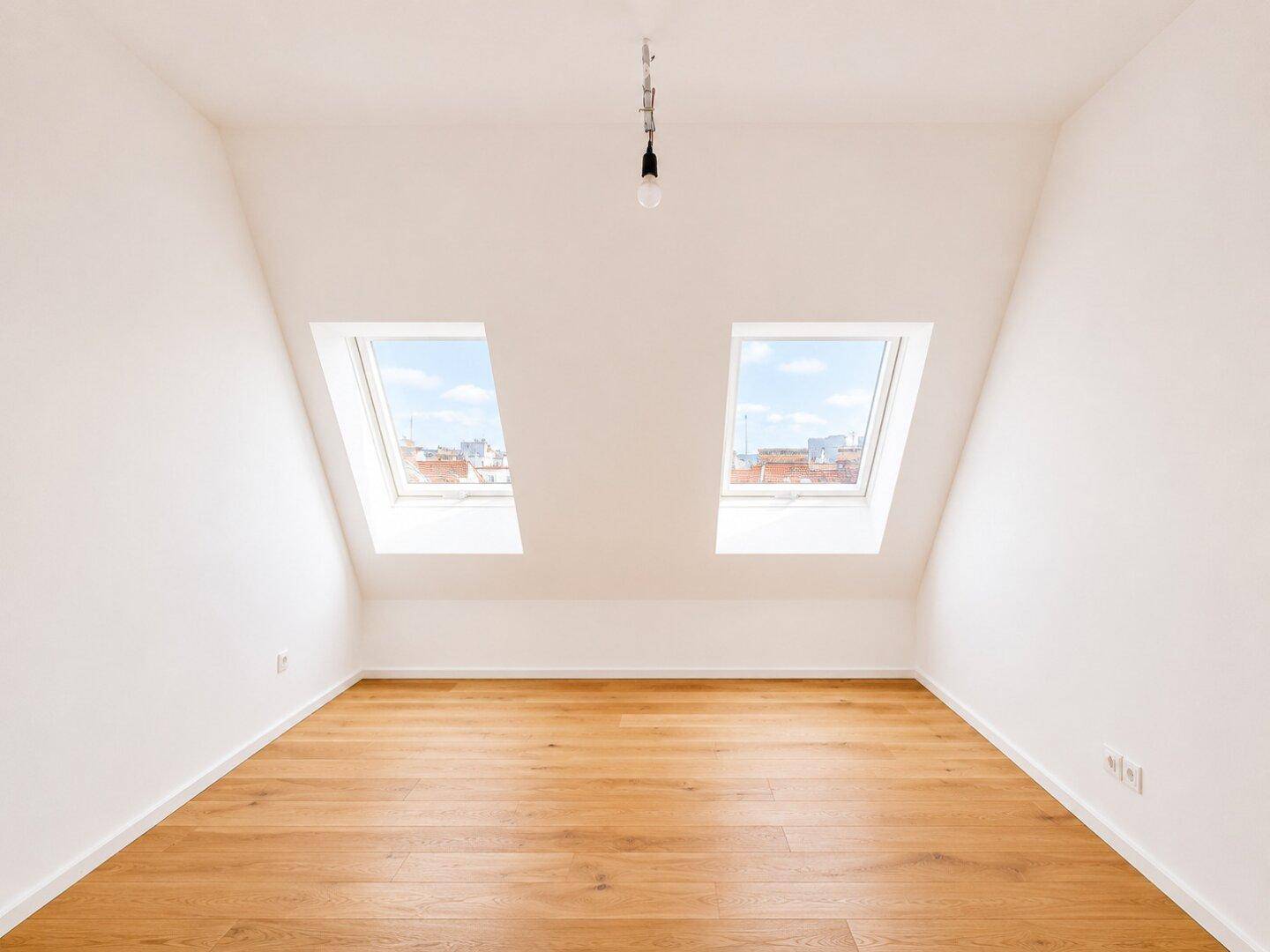 Leerer Raum im Dachgeschoss mit zwei Dachfenstern und hellem Holzboden, bietet viel natürliches Licht.