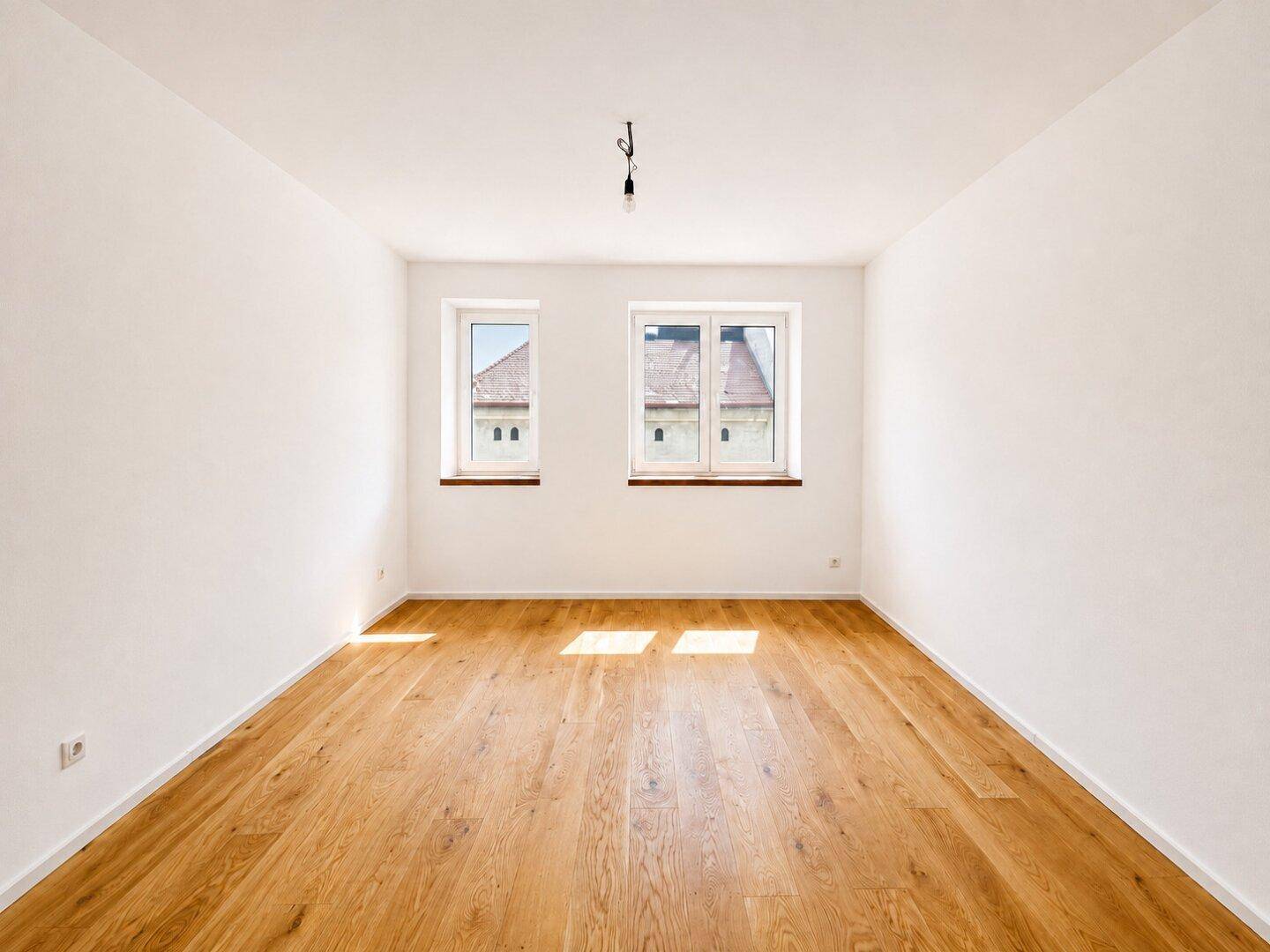 Heller, leerer Raum mit zwei Fenstern und Holzboden, bietet eine neutrale Basis für individuelle Gestaltung.