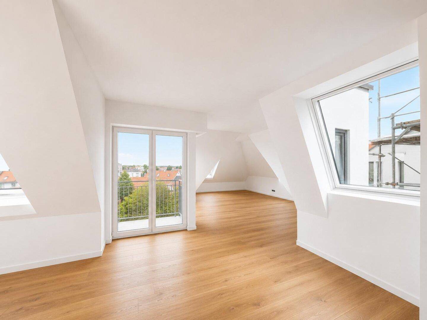 Großer, unmöblierter Raum mit Holzboden, Dachschrägen und Zugang zu zwei Balkonen.