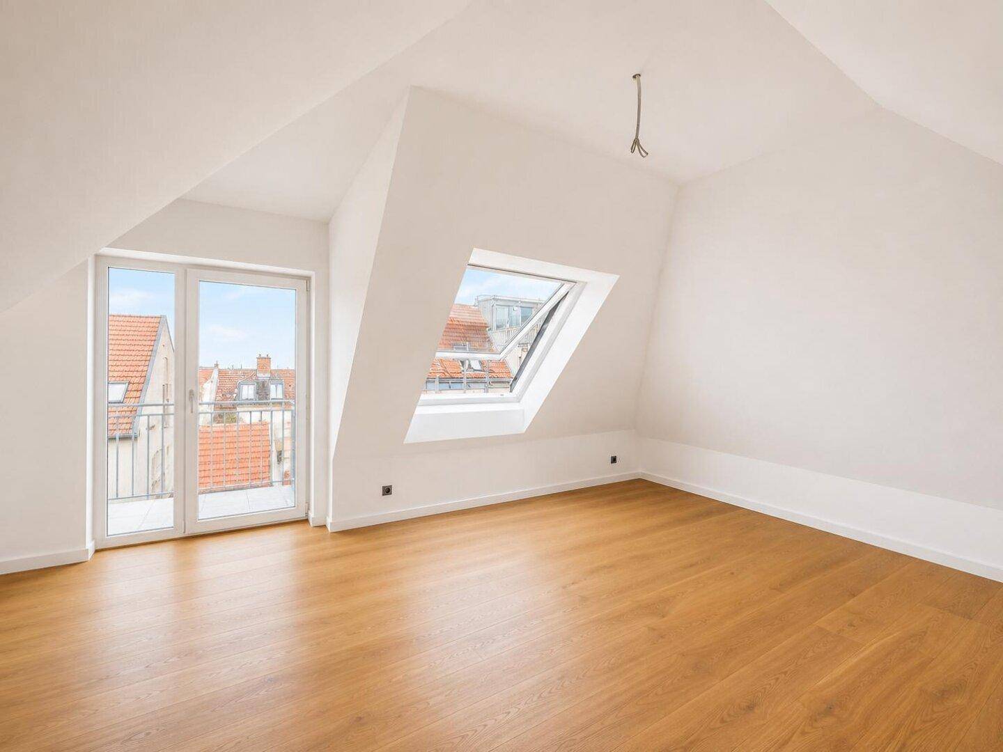 Leeres Wohnzimmer im Dachgeschoss mit Holzboden, Balkonzugang und Dachfenster.