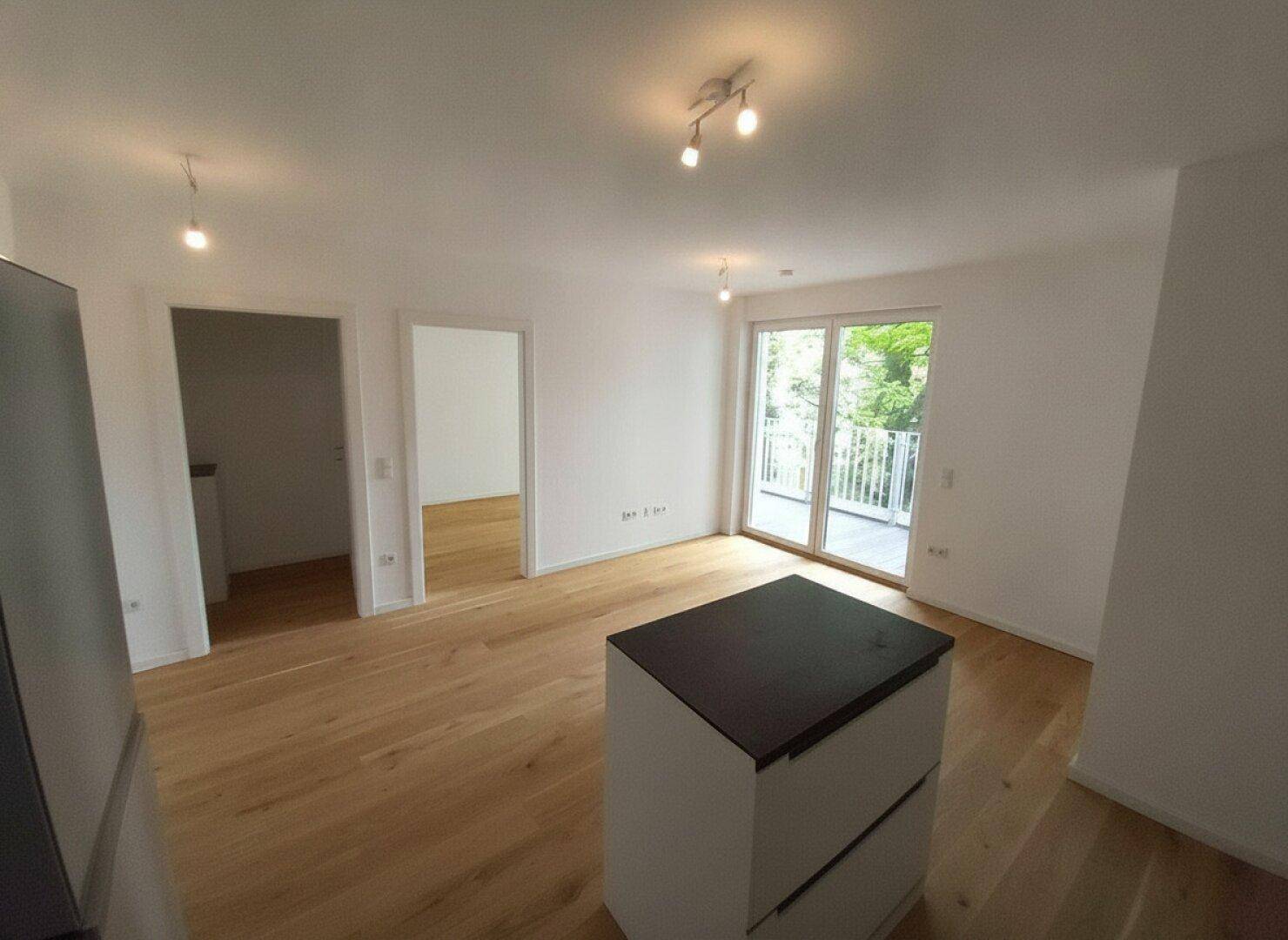 Heller, leerer Wohnraum mit Holzboden und großem Schiebetürzugang zu einem Balkon.