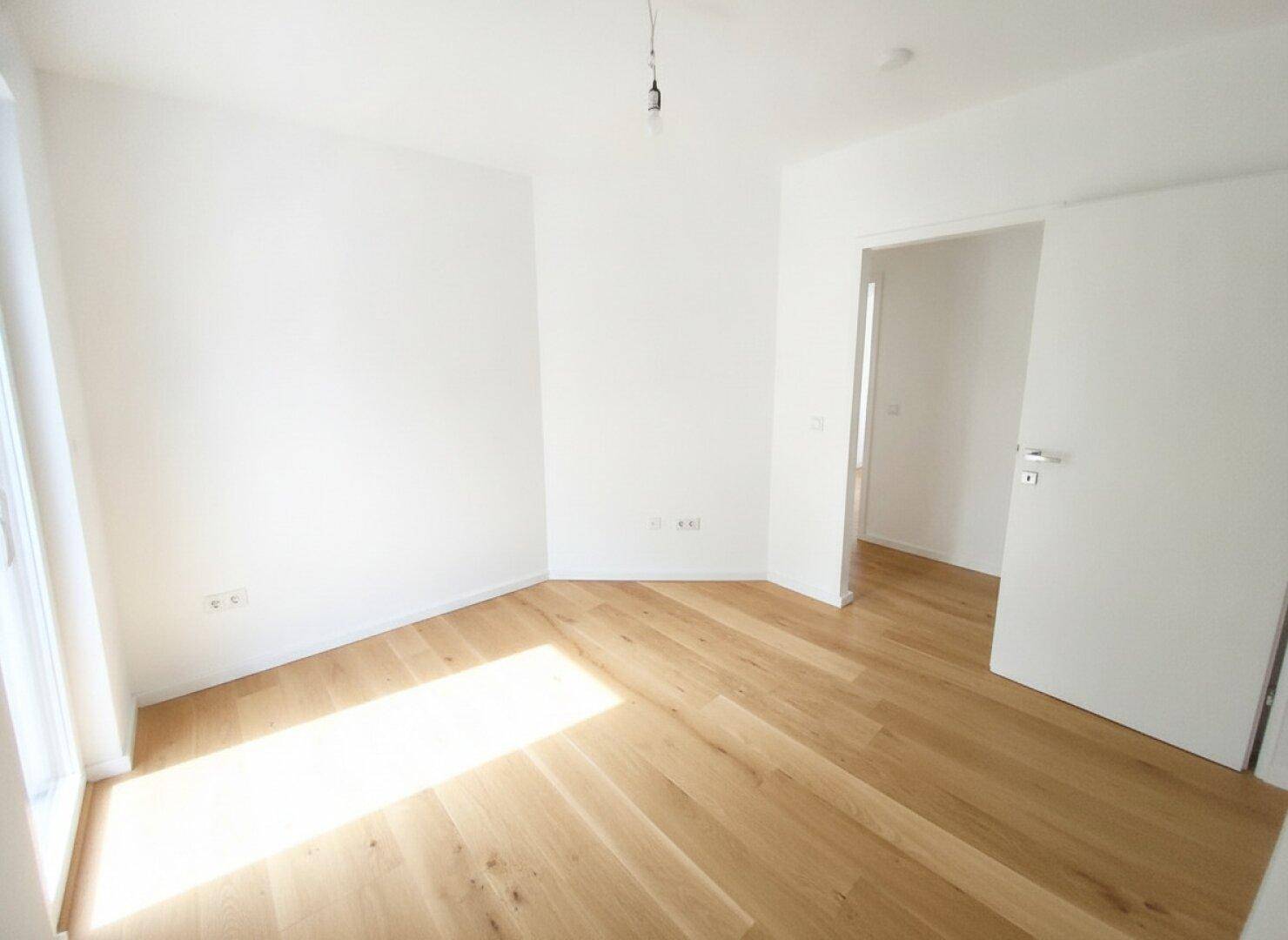 Helles, leeres Zimmer mit Holzboden und viel natürlichem Licht durch das Fenster.