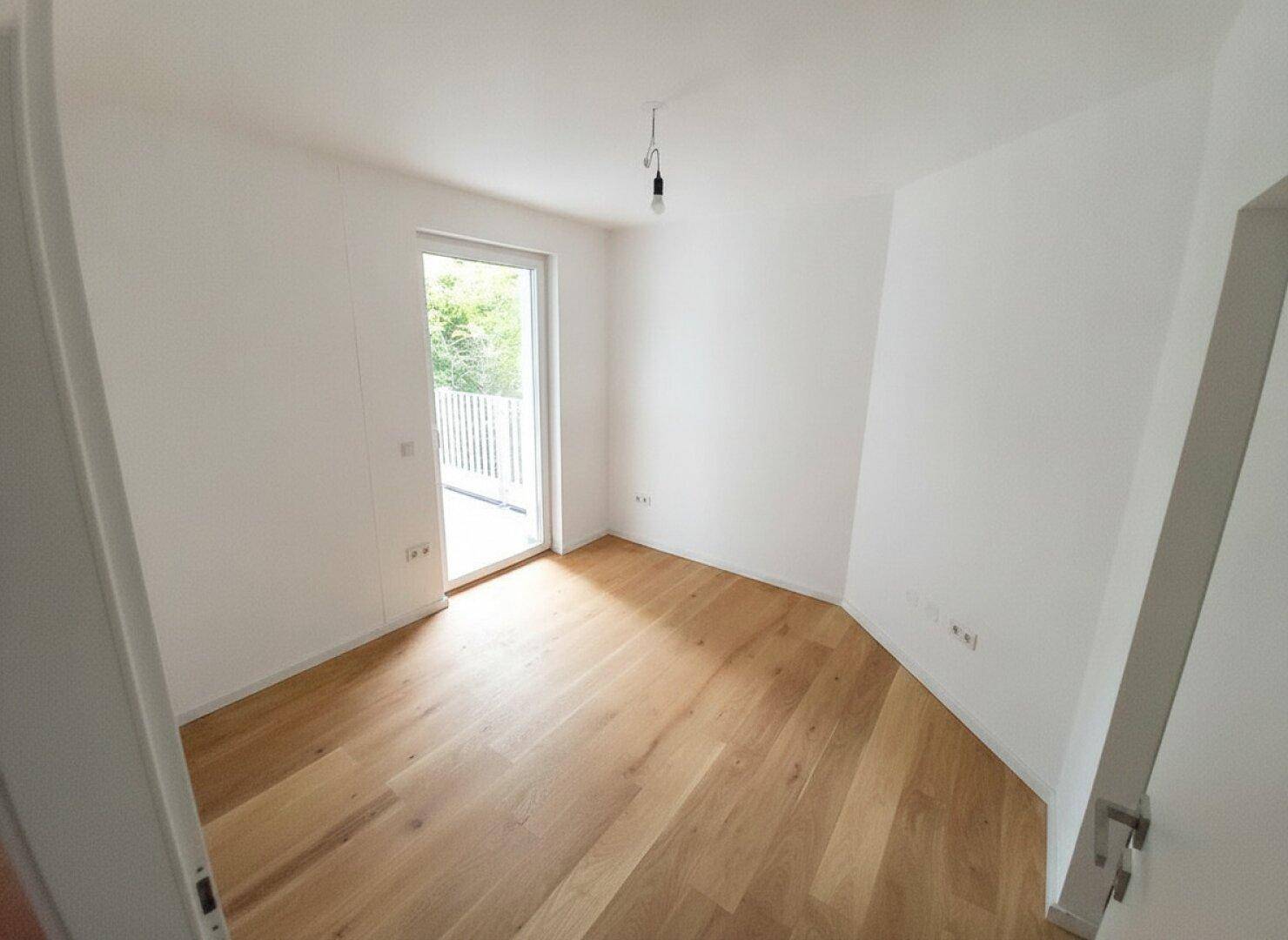 Leeres Schlafzimmer mit Holzboden und direktem Zugang zu einem kleinen Balkon.