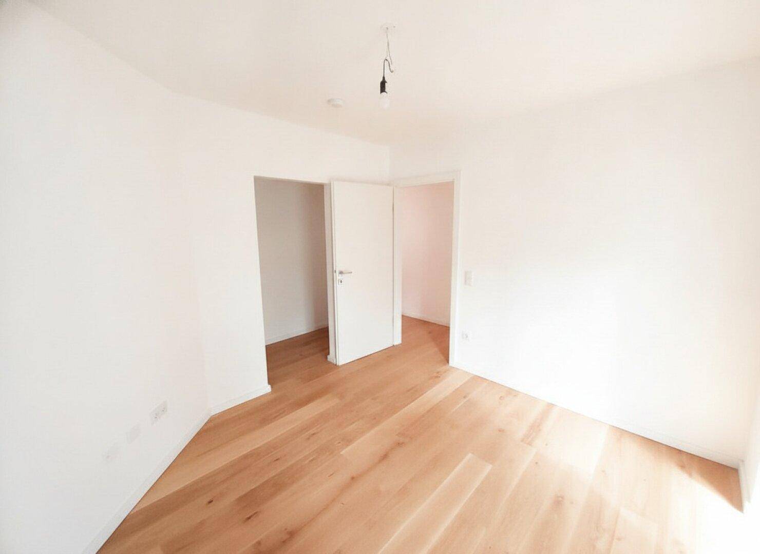 Leeres Zimmer mit Holzboden und zwei Türen, das vielseitig genutzt werden kann.