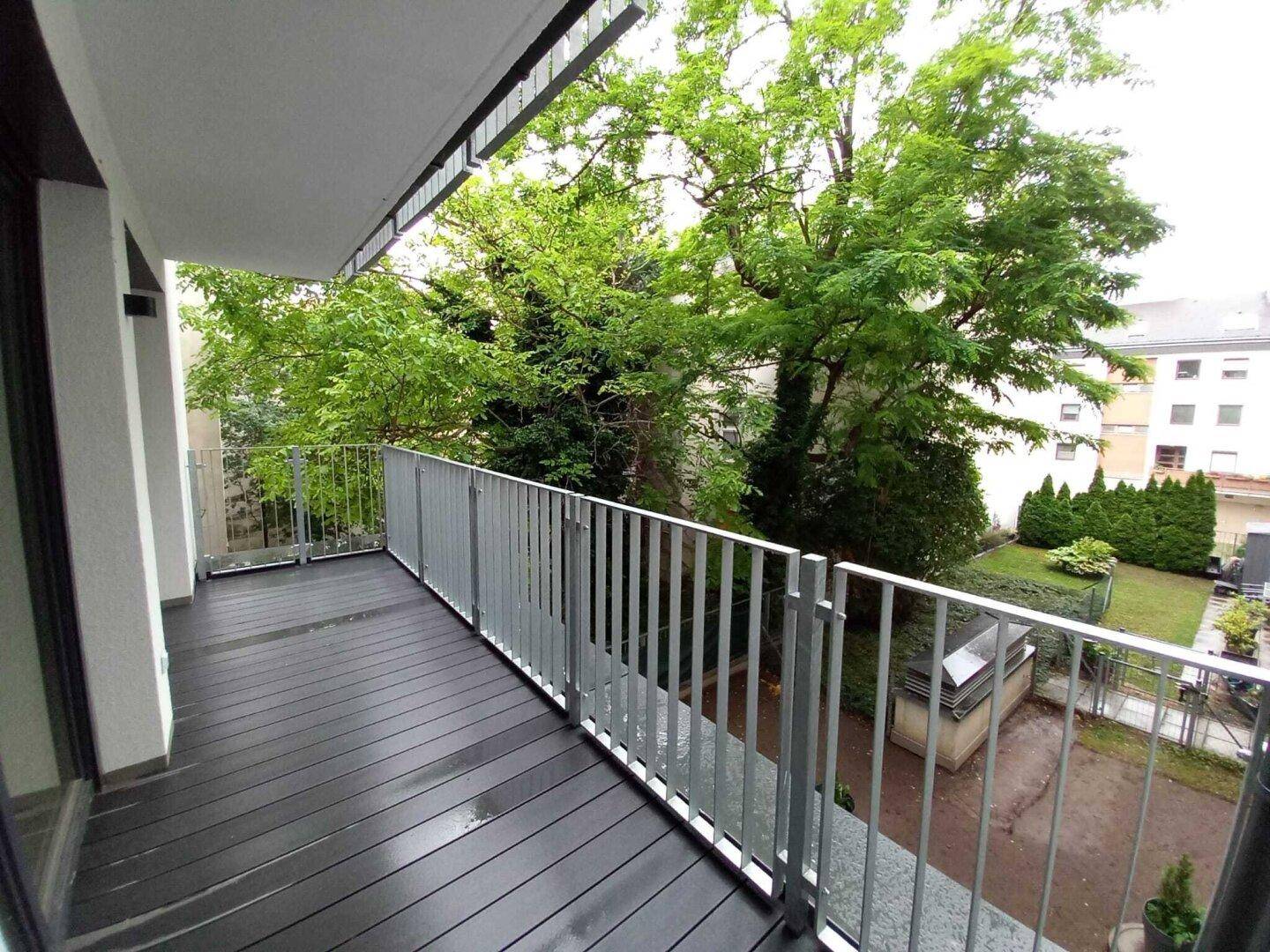 Geräumiger Balkon mit dunklem Holzboden und grünem Ausblick auf Bäume und Garten.
