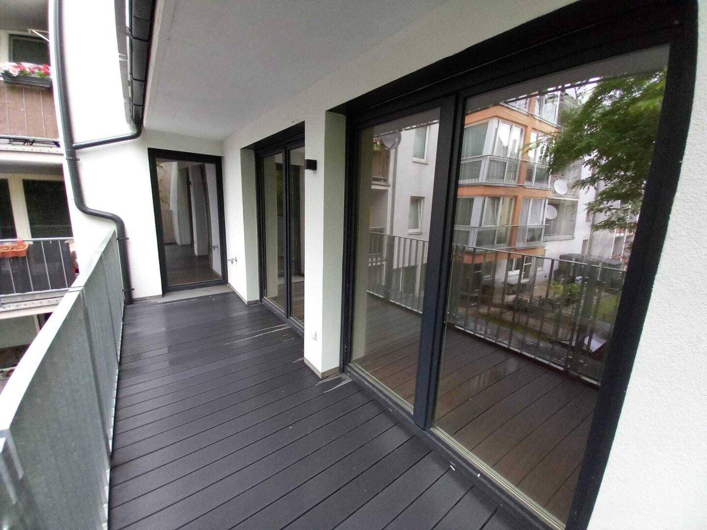 Moderner Balkon mit dunklem Holzboden und Blick auf die umliegenden Gebäude.
