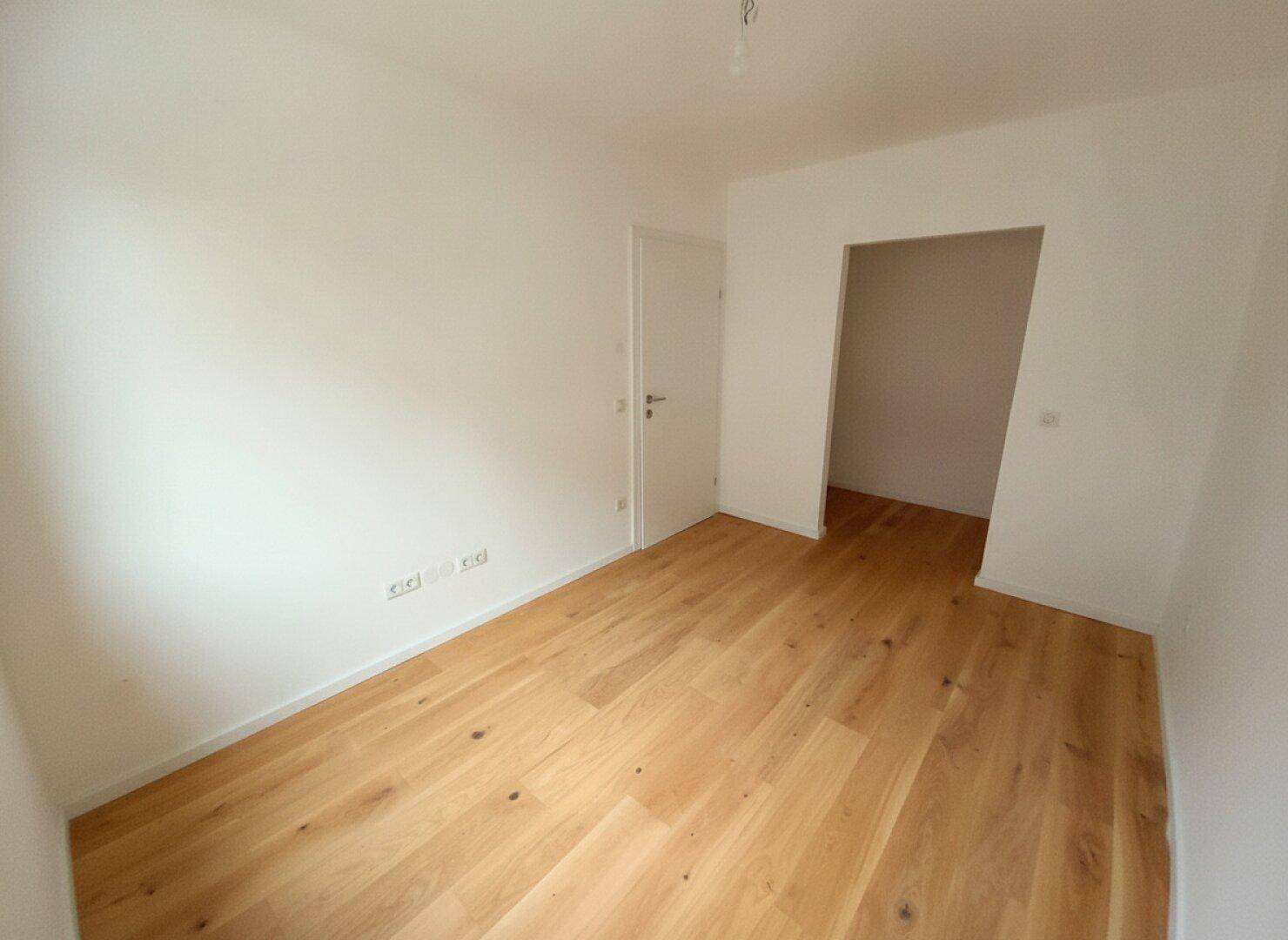 Geräumiger, unmöblierter Raum mit Holzboden und Zugang zu weiteren Zimmern.
