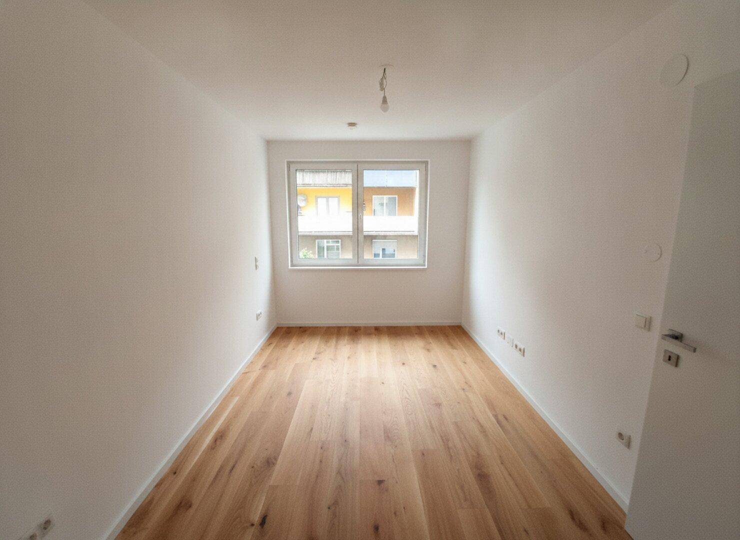 Heller, leerer Raum mit neuem Holzfußboden und Blick auf Nachbargebäude.